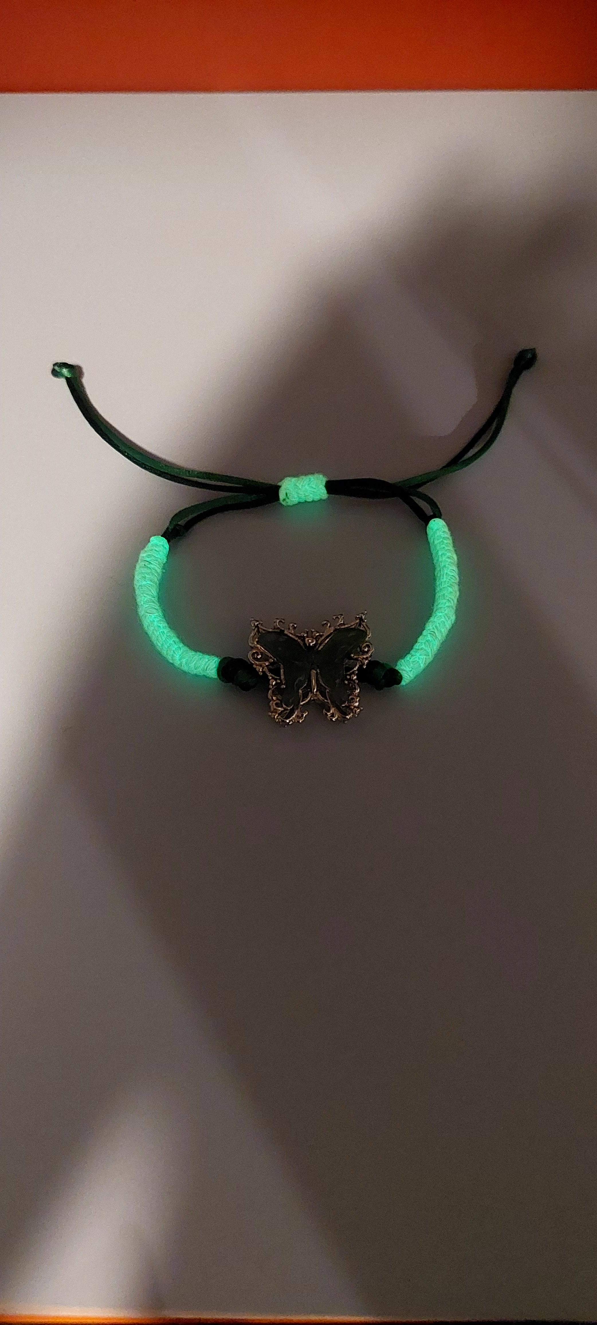 Adjustable bracelet with a satin cord and a butterfly-shaped charm, predominantly green and white in color. with glow in the dark cord