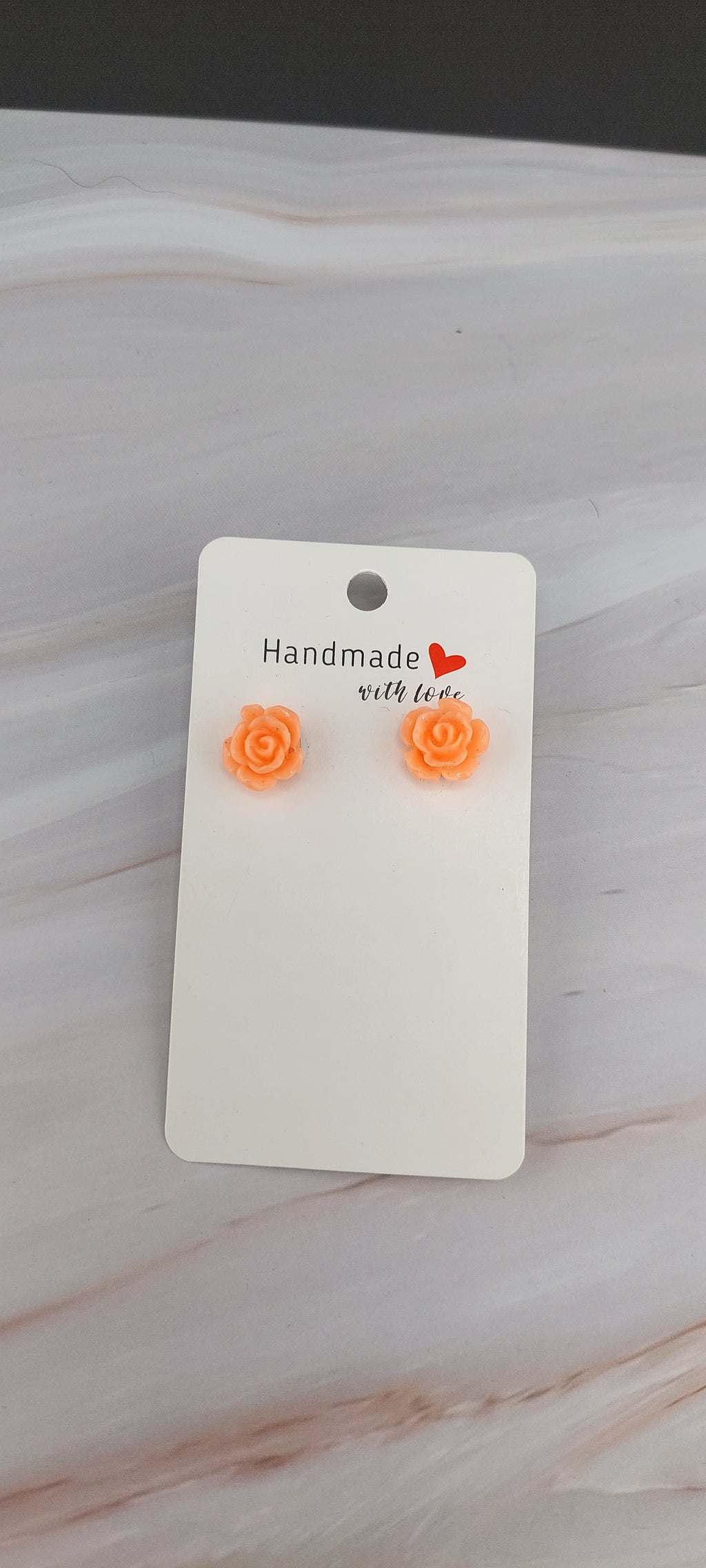 A pair of gold-colored rose stud earrings displayed on a black backing card.