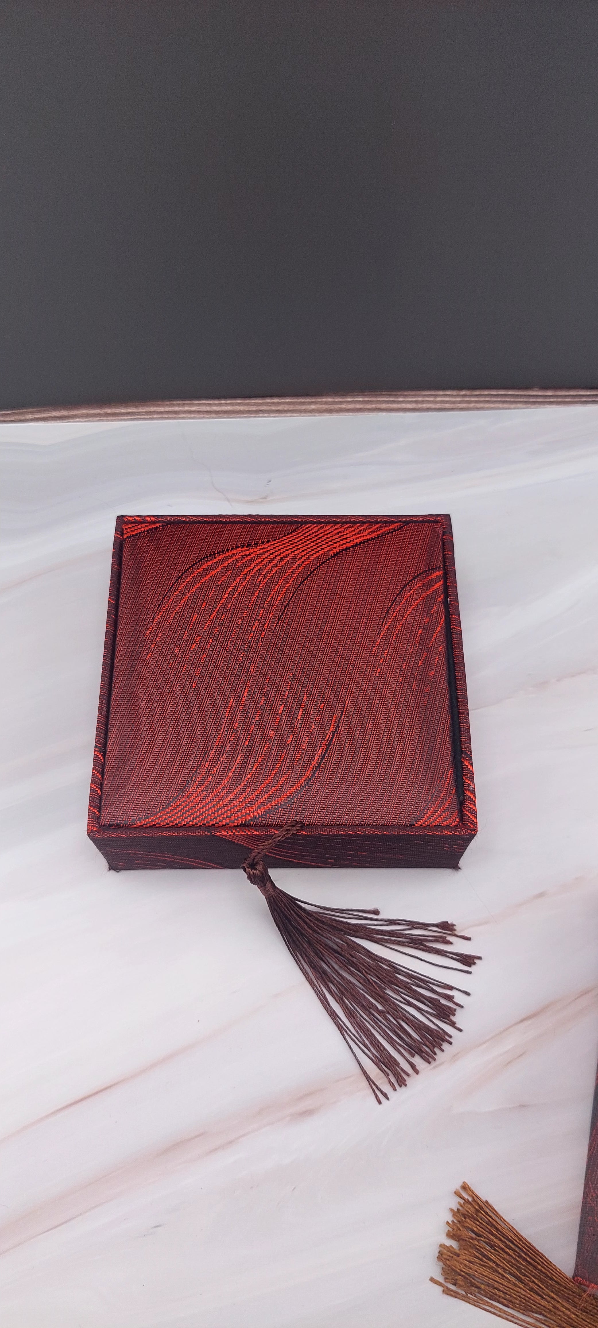 A red Chinese bangle box with a decorative pattern and a tassel on the front.