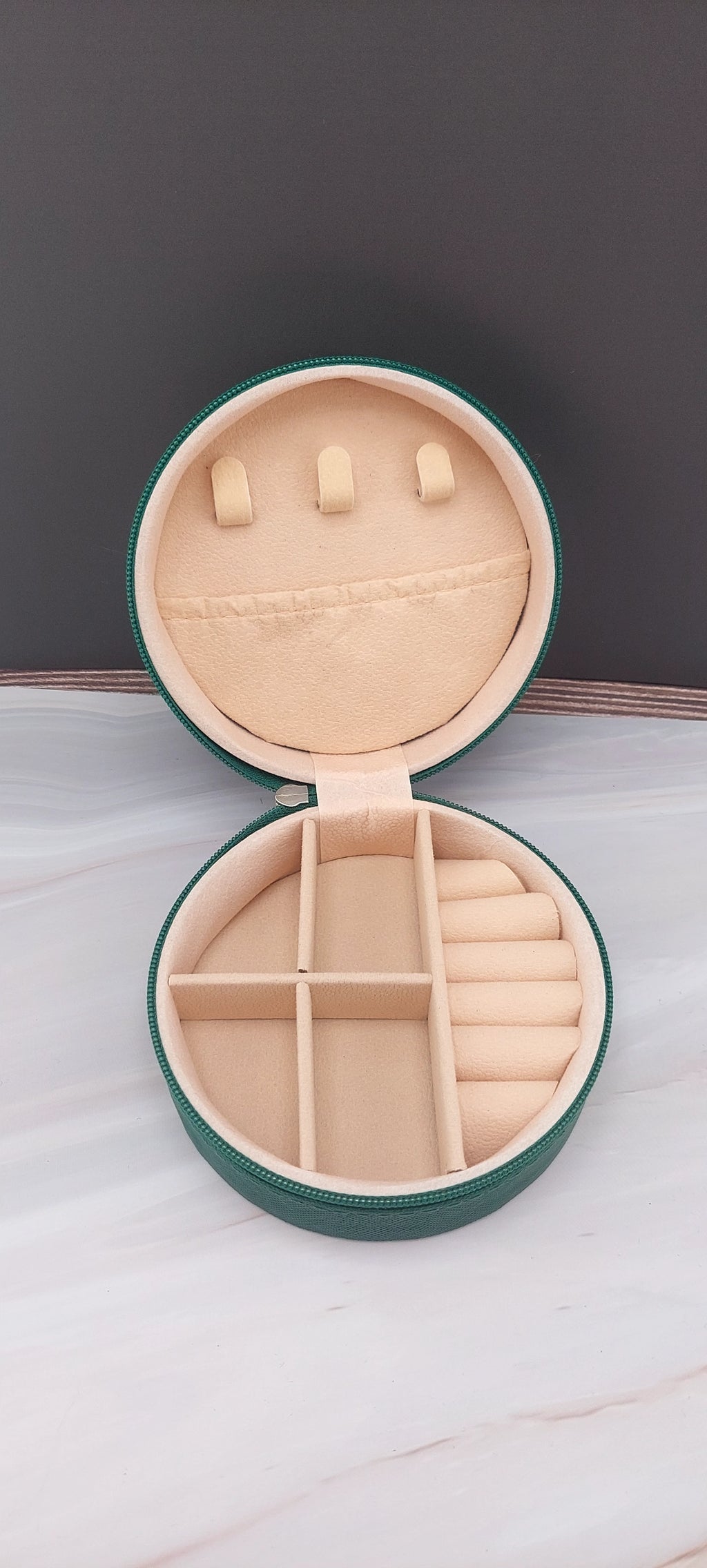 A round jewelry box with a beige interior and patterned exterior, partially open, showing its compartments.