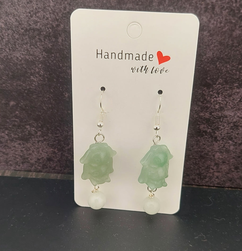 Green earrings on a 'Handmade with Love' card against a dark background
