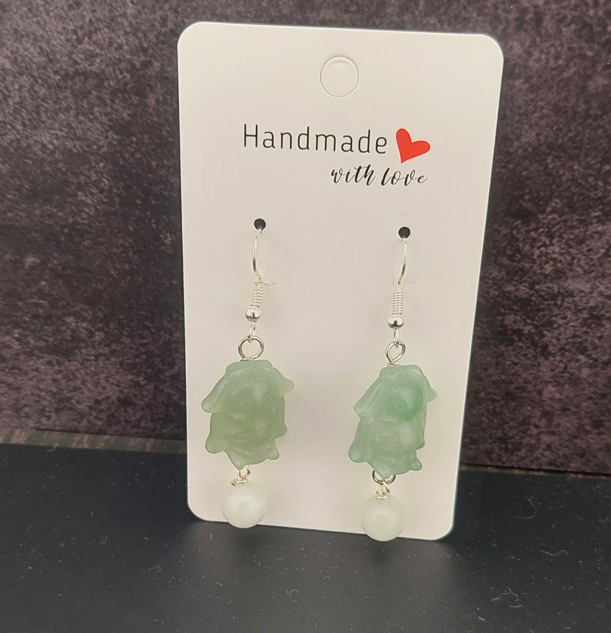 Green earrings on a 'Handmade with Love' card against a dark background