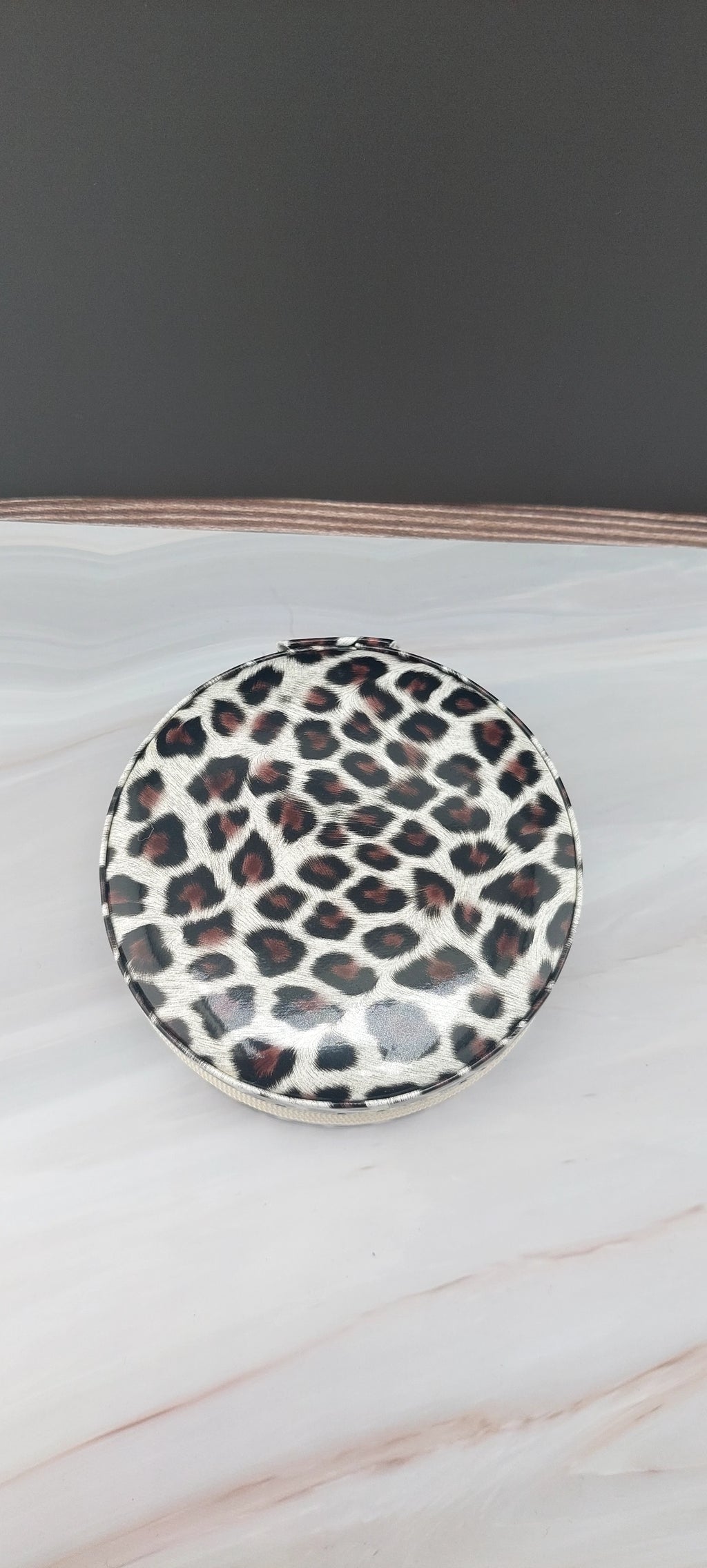 A round jewelry box with a beige interior and patterned exterior, partially open, showing its compartments.