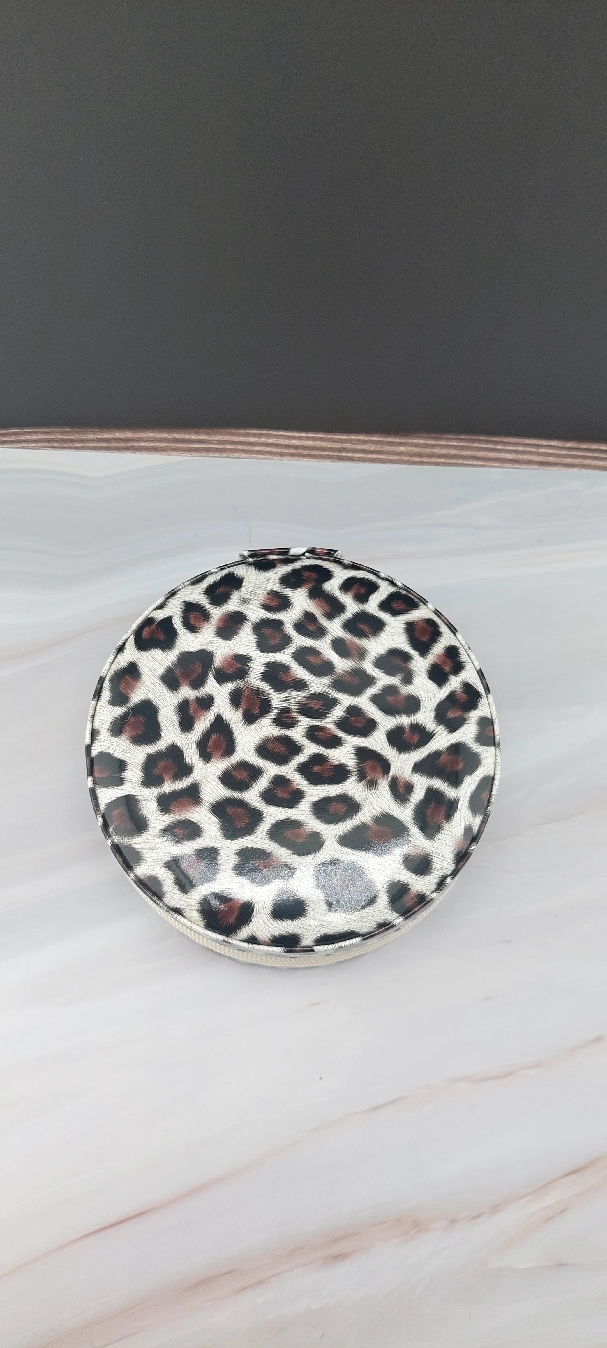 A round jewelry box with a beige interior and patterned exterior, partially open, showing its compartments.