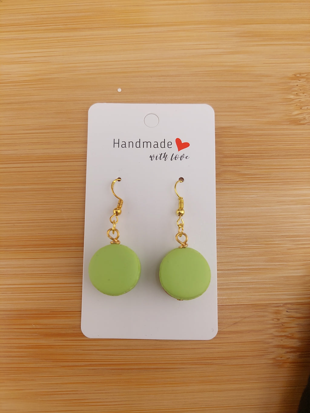 Green earrings on a white card with 'Handmade with Love' text, placed on a wooden surface.