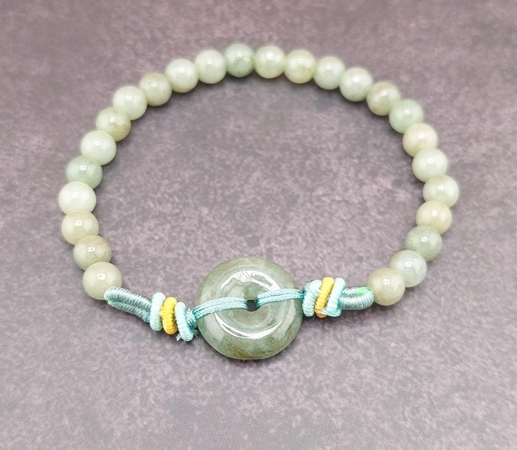 A bracelet made of round blue water jade stones with gold accents and a blue fabric tie at the clasp, featuring a small circular silver charm.