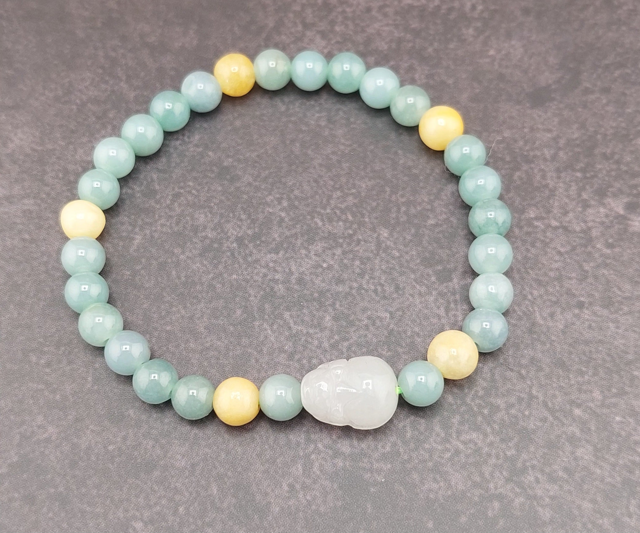 A bracelet made of round blue water jade stones with gold accents and a blue fabric tie at the clasp, featuring a small circular silver charm.