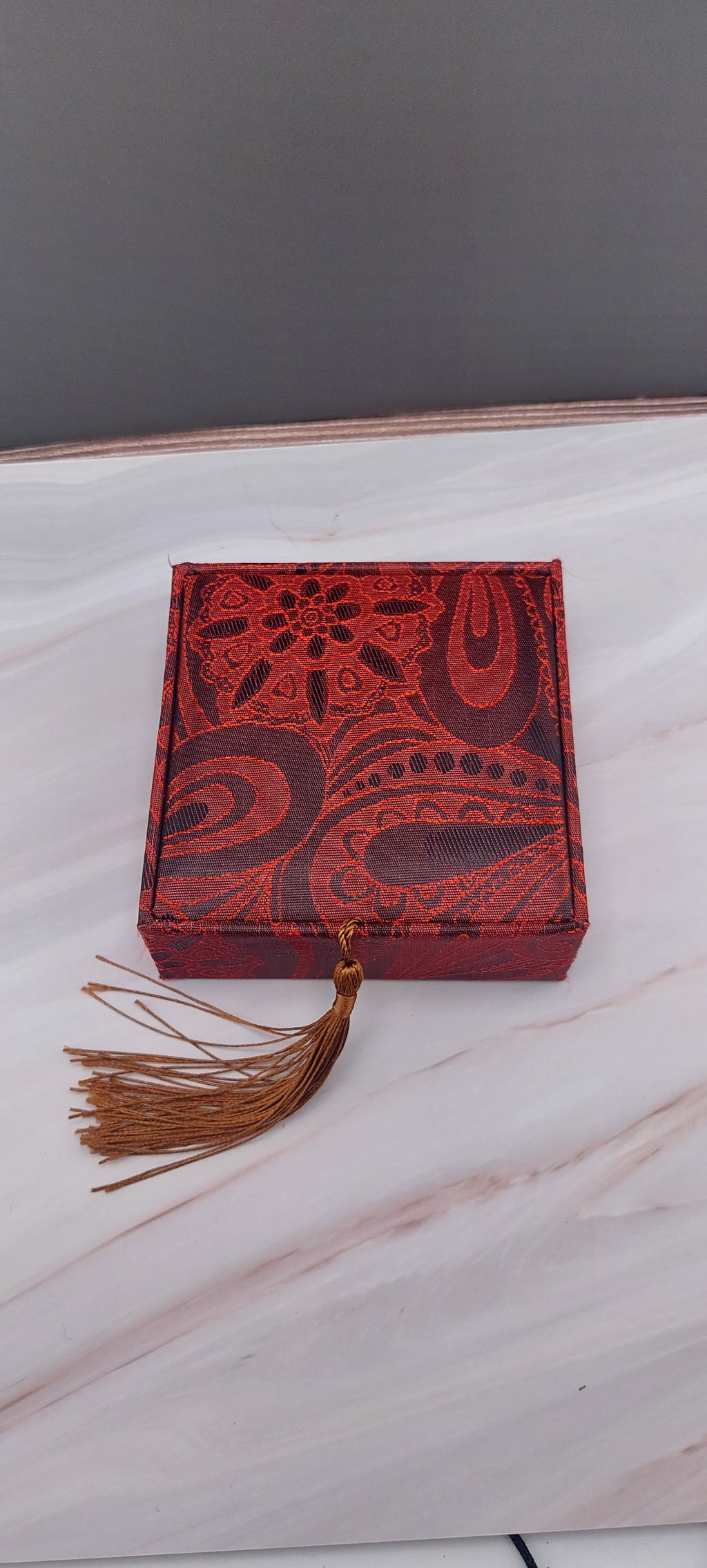 A red Chinese bangle box with a decorative pattern and a tassel on the front.