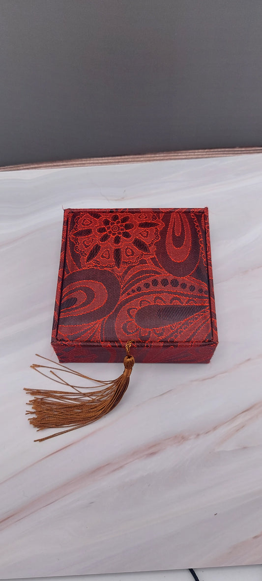 A red Chinese bangle box with a decorative pattern and a tassel on the front.