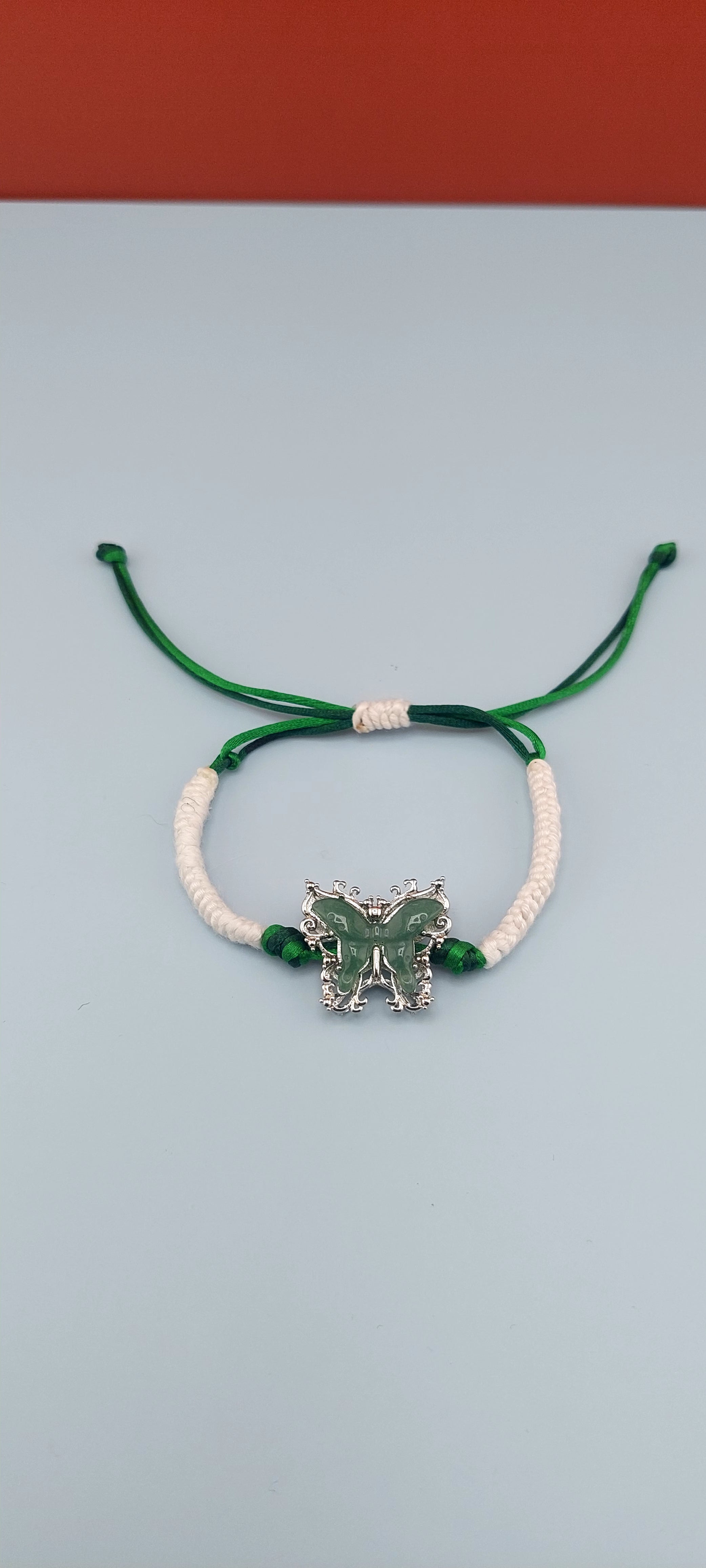 Adjustable bracelet with a satin cord and a butterfly-shaped charm, predominantly green and white in color.