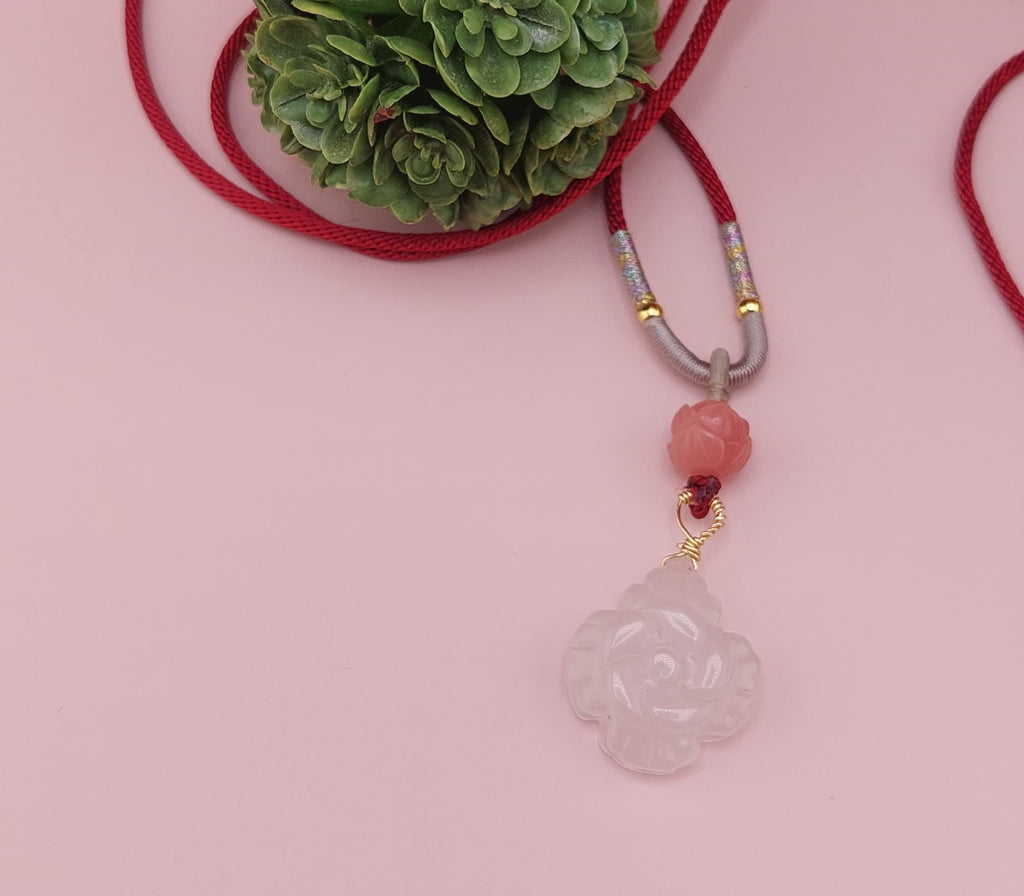 A colorful agate flower necklace with a red cord and a floral pattern on the agate stone, displayed against a pink background with a decorative green item in the background.
