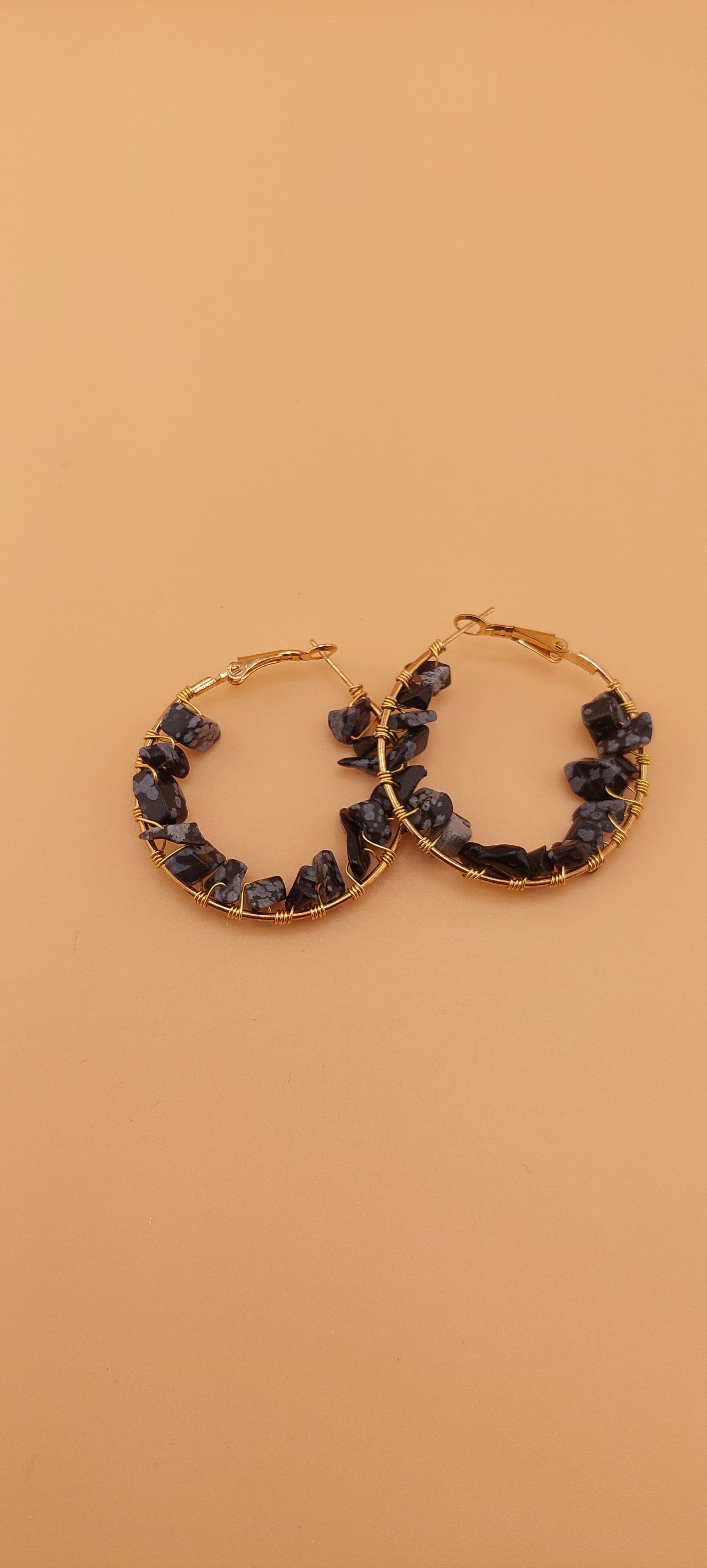 A pair of gold-colored hoop earrings adorned with blue gemstones, displayed against a beige background