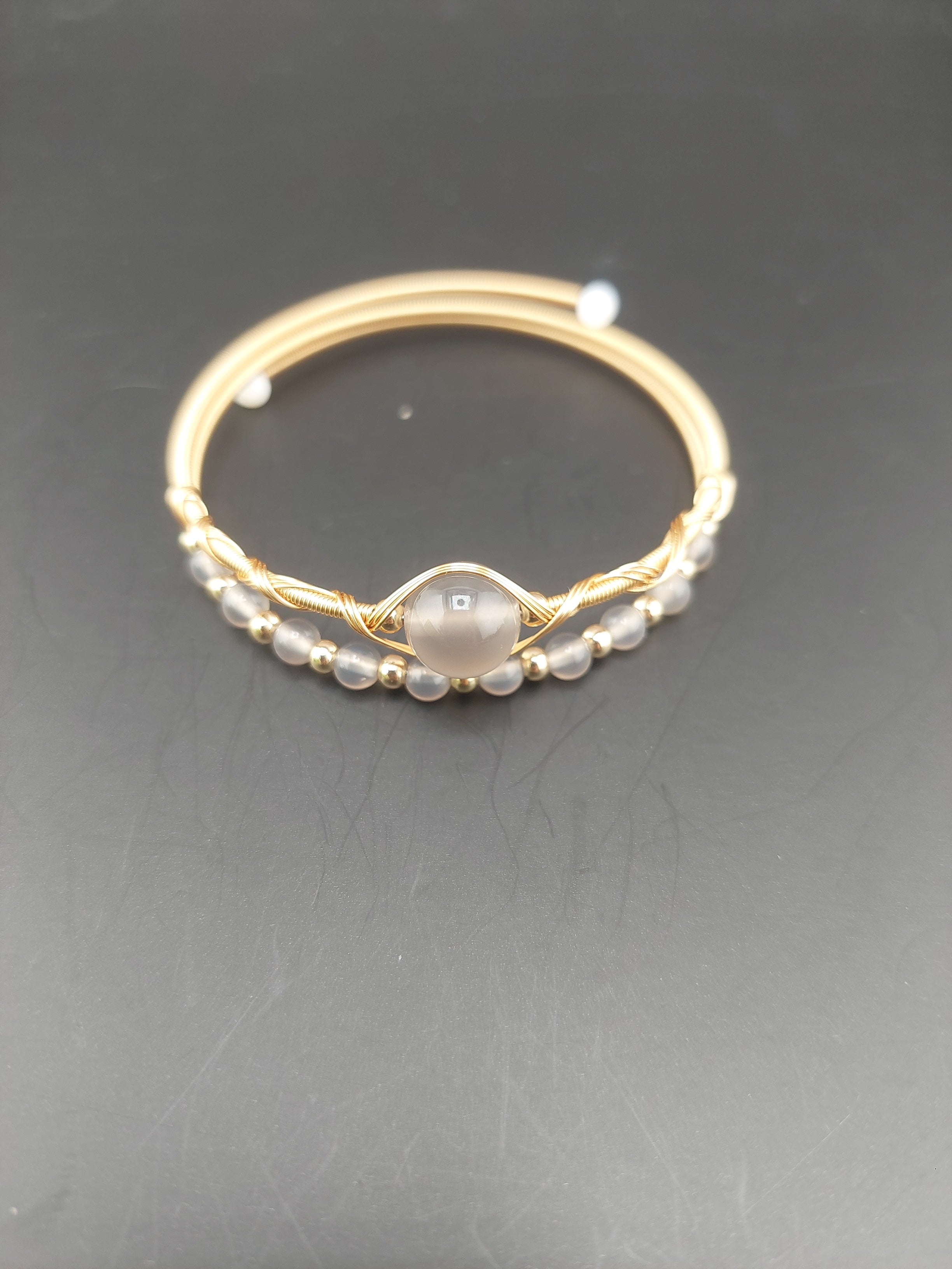 Gold wire wrapped with a central gemstone and pearl-like accents on a dark background