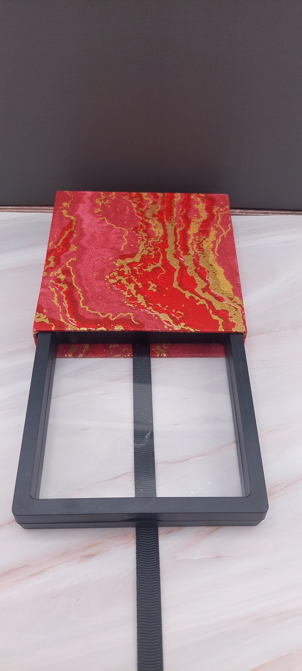 A red and gold bangle box with a sticky texture on the inside, placed on a marble surface.