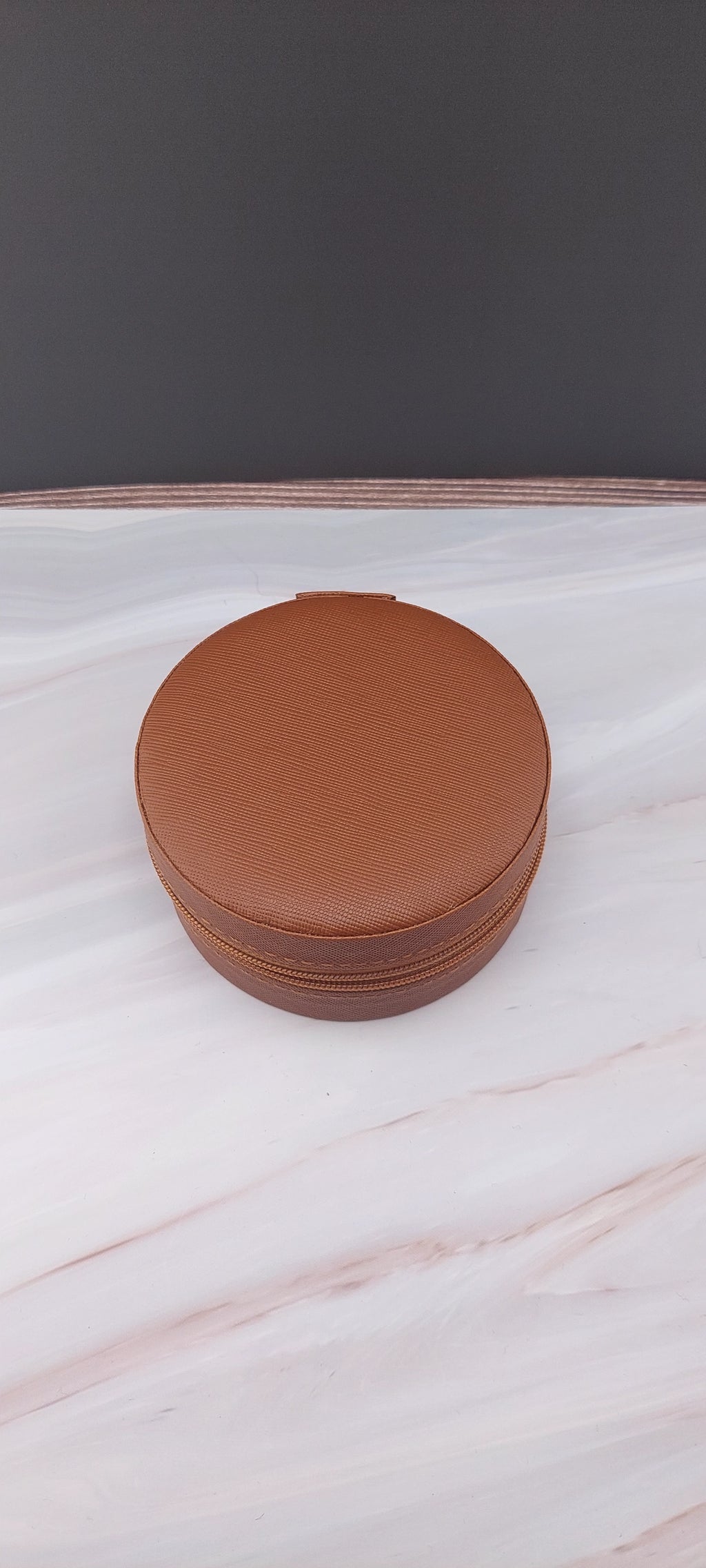 A round jewelry box with a beige interior and patterned exterior, partially open, showing its compartments.