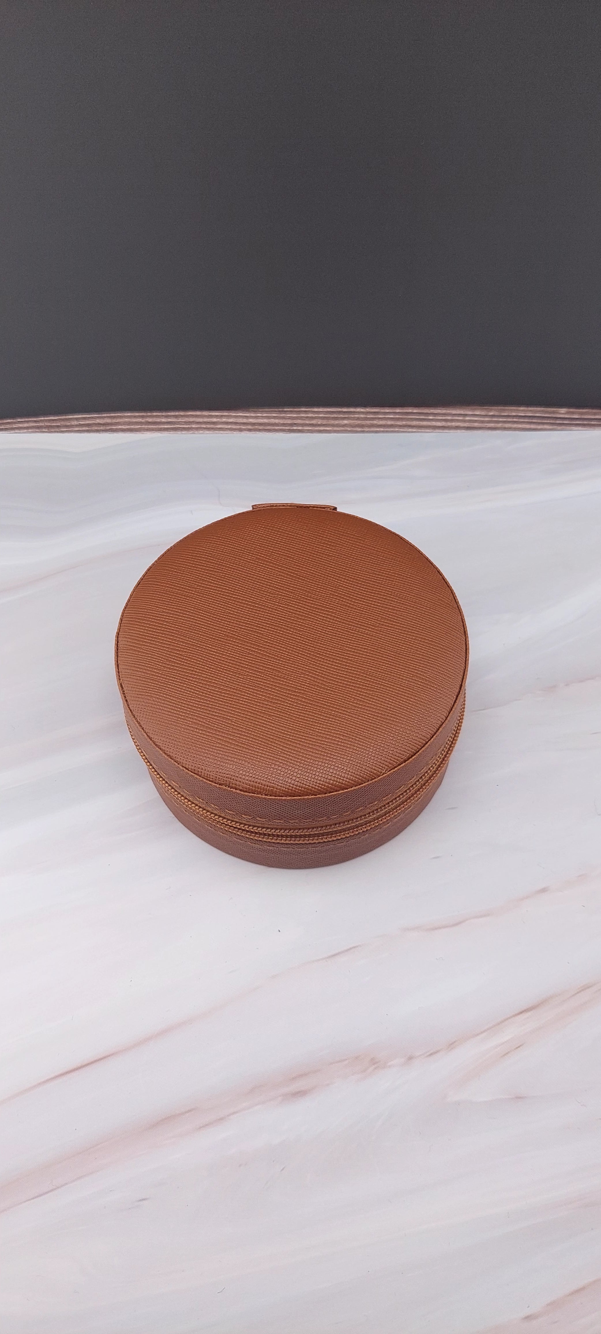 A round jewelry box with a beige interior and patterned exterior, partially open, showing its compartments.