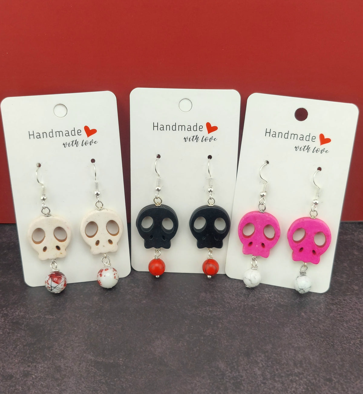 Set of skull-shaped earrings on cards with 'Handmade with Love' text against a red background.
