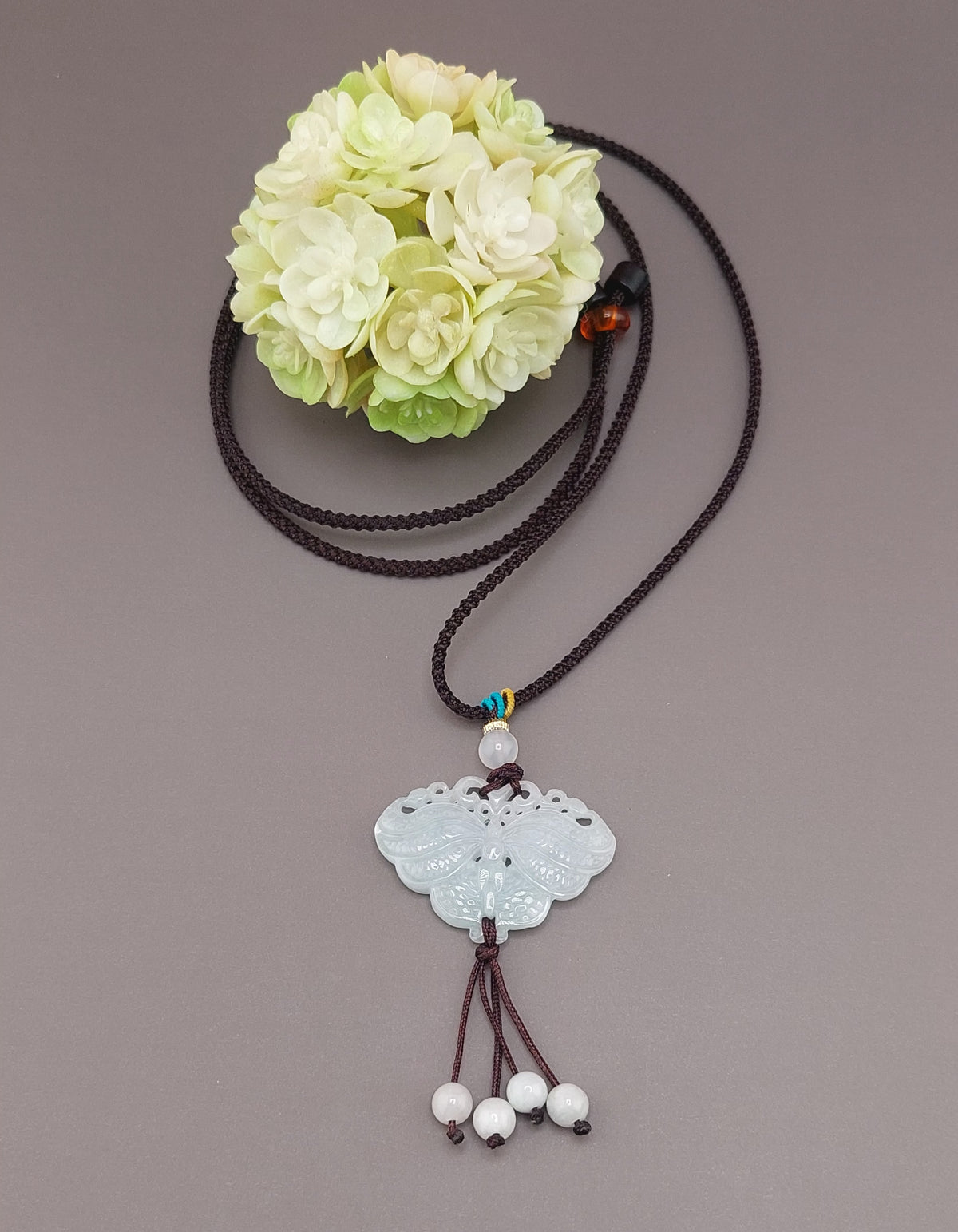 A blue water jade butterfly necklace displayed against a neutral background with a floral patterned object to the side.