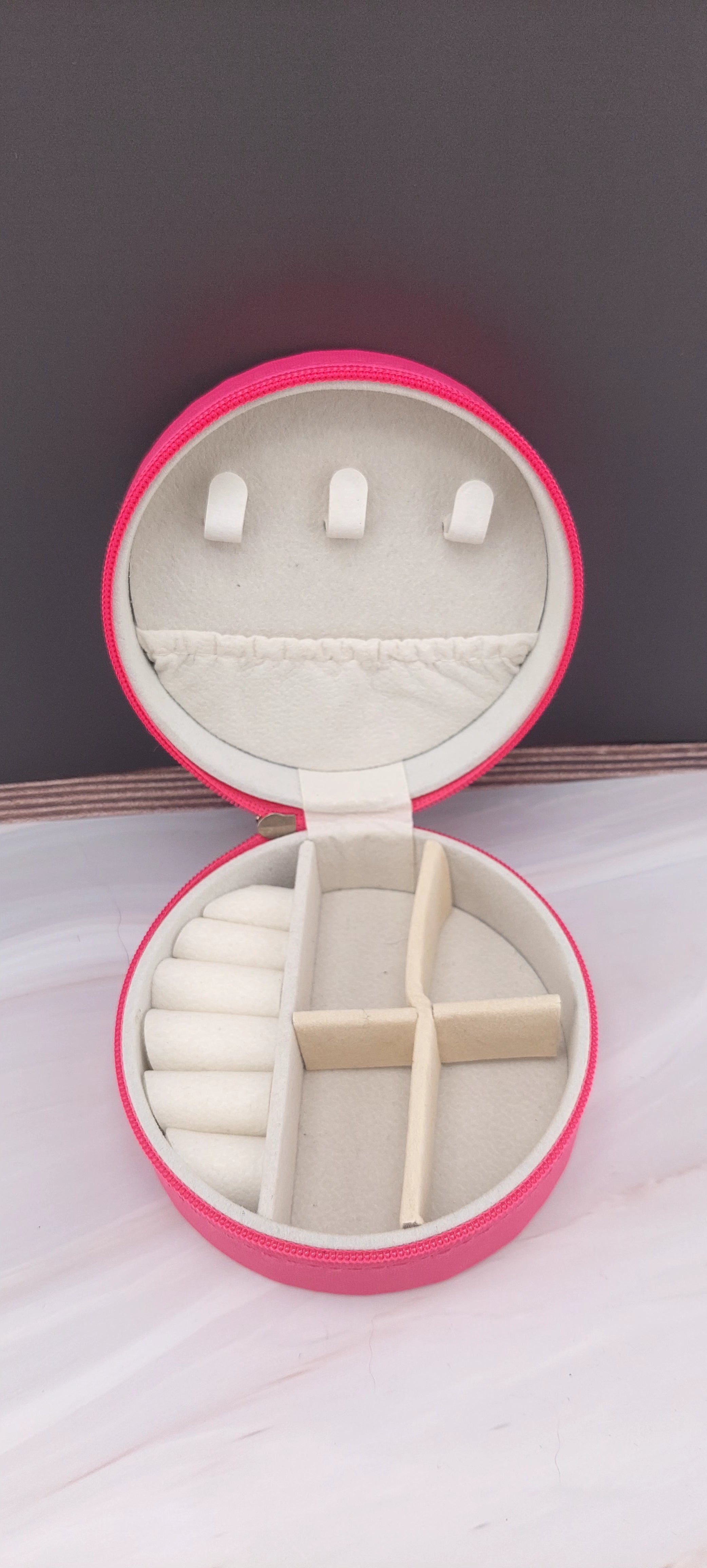 A round jewelry box with a beige interior and patterned exterior, partially open, showing its compartments.