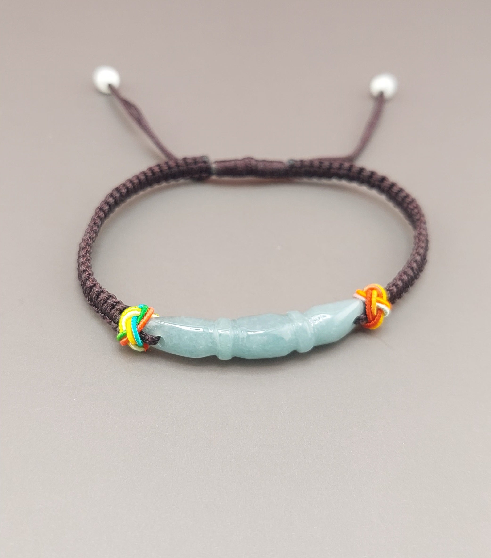 A macrame bracelet with a blue water jade pendant, featuring colorful tassels on the sides.