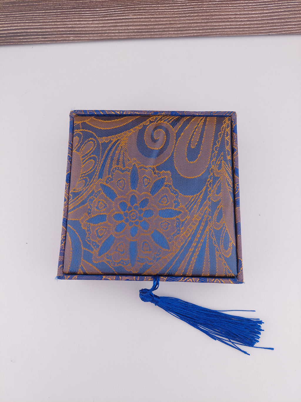 Decorative box with blue and gold pattern and a blue tassel on a white background