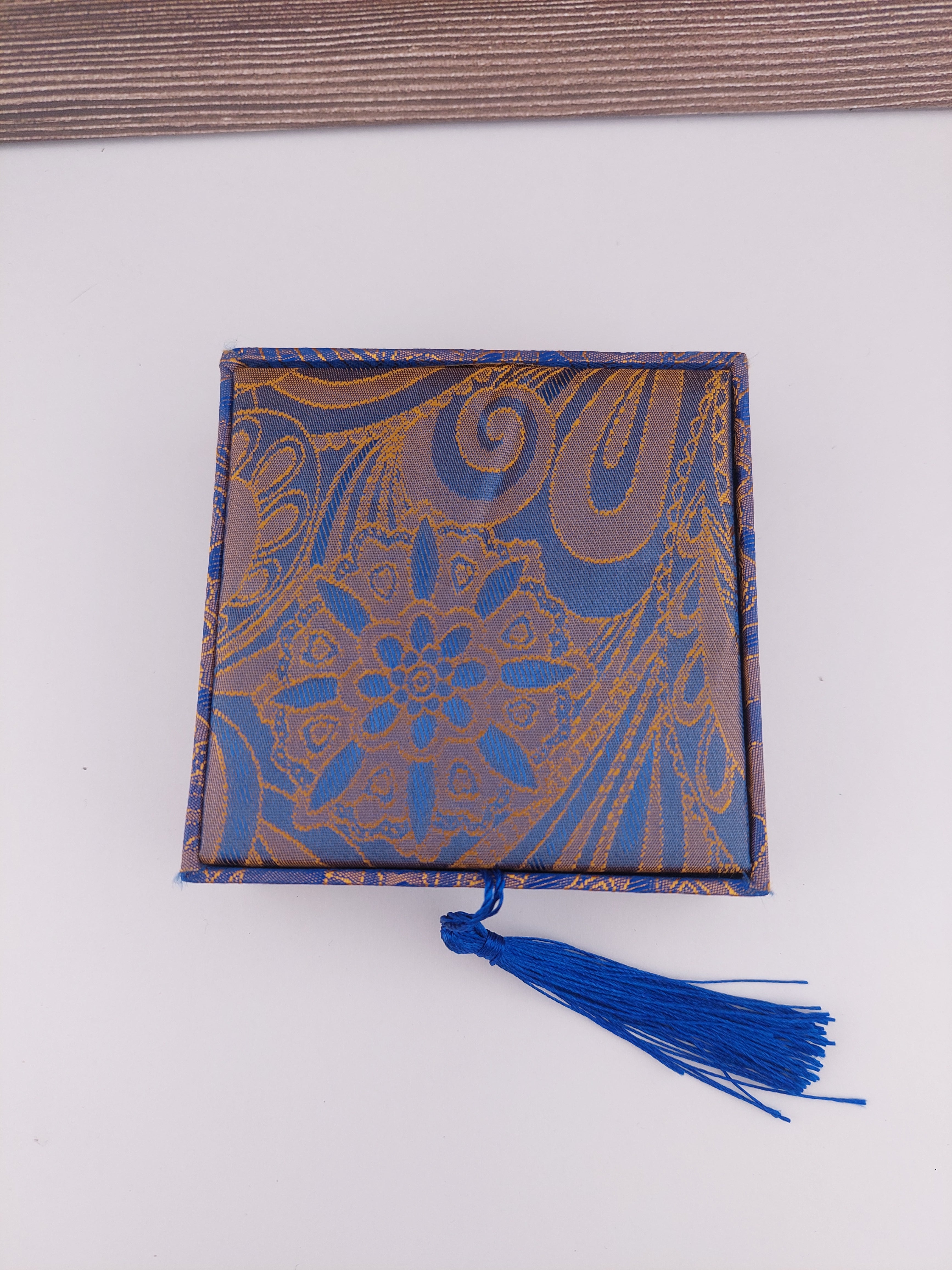 Decorative box with blue and gold pattern and a blue tassel on a white background