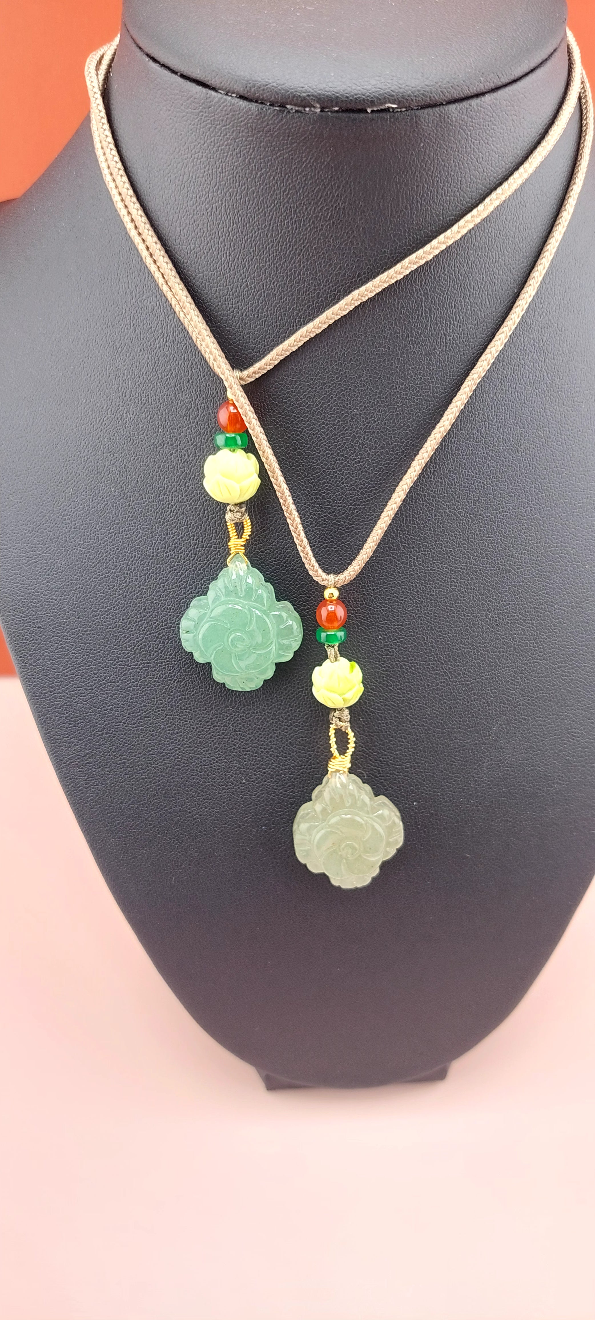 A colorful agate flower necklace with a red cord and a floral pattern on the agate stone, displayed against a pink background with a decorative green item in the background.