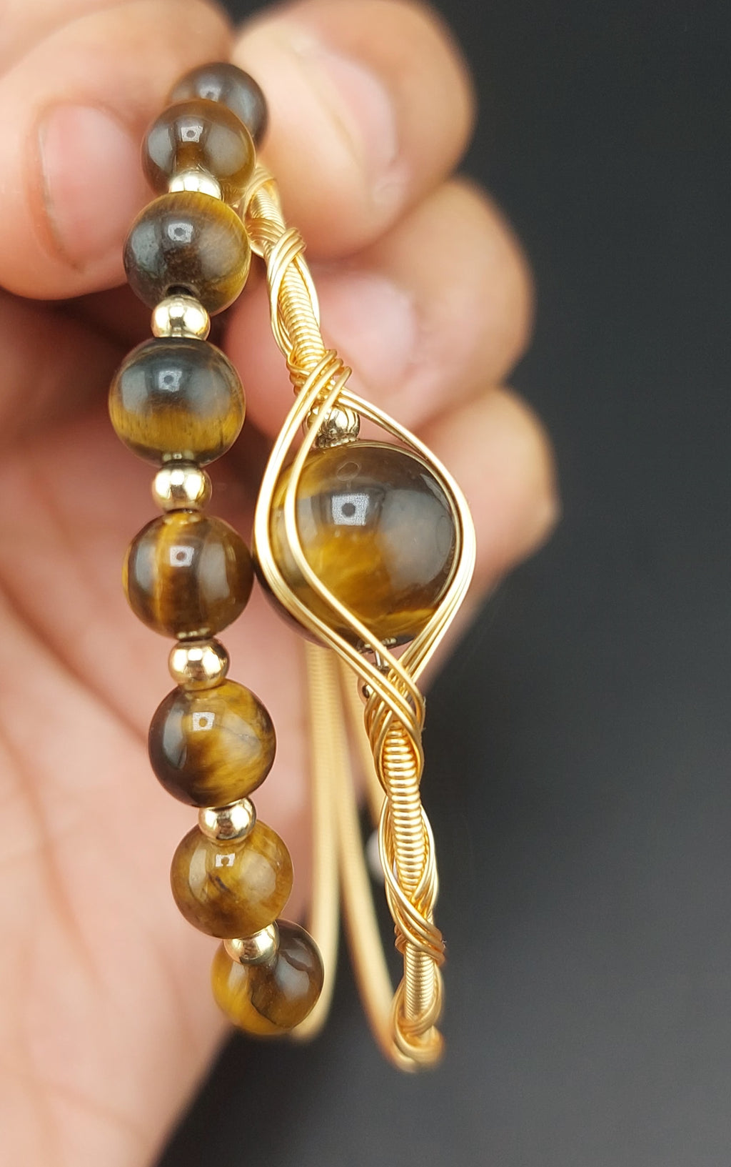 Gold bracelet with tiger's eye beads held in a hand against a dark background