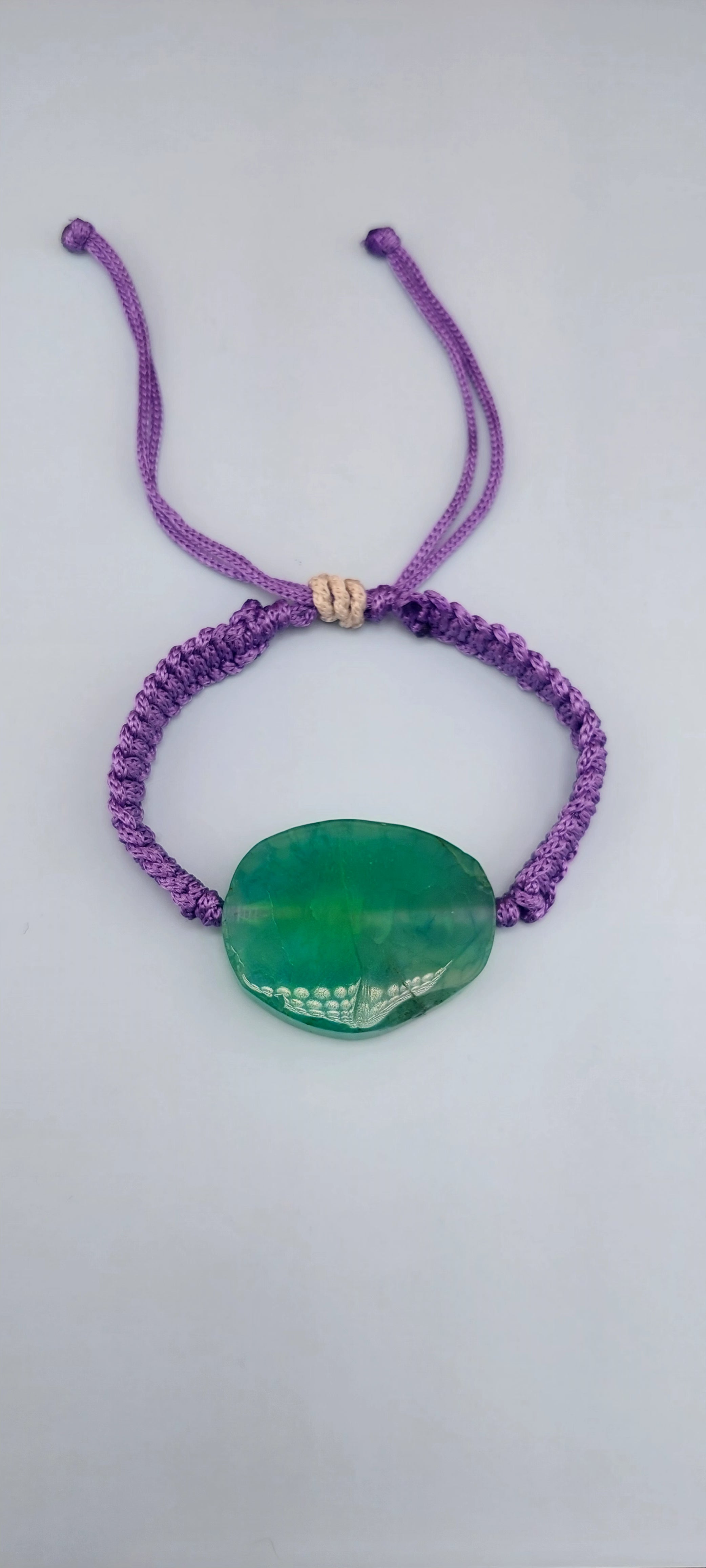 Adjustable green adventurine macrame bracelet with a purple cord and a green stone pendant, displayed against a white background.
