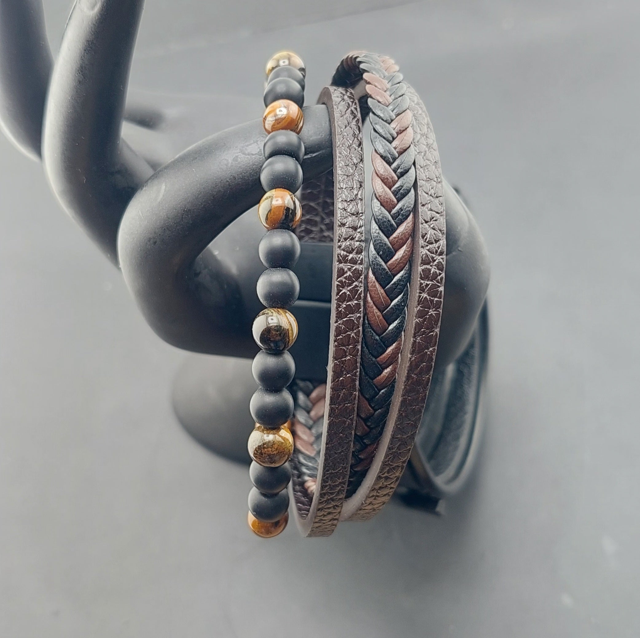 Two bracelets, one with beads and the other with braided design, on a gray surface.