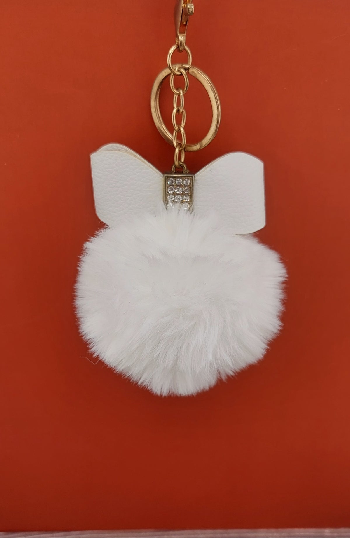 White fluffy keychain with gold ring on a red background
