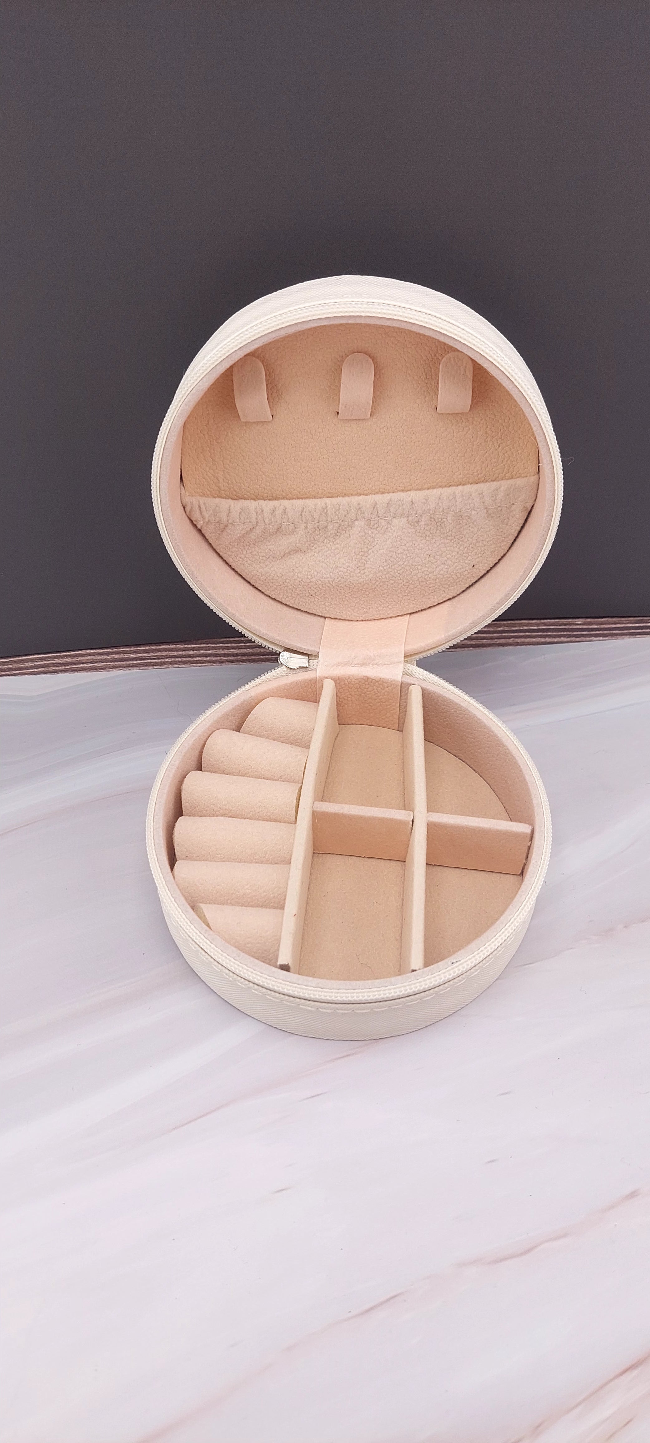 A round jewelry box with a beige interior and patterned exterior, partially open, showing its compartments.
