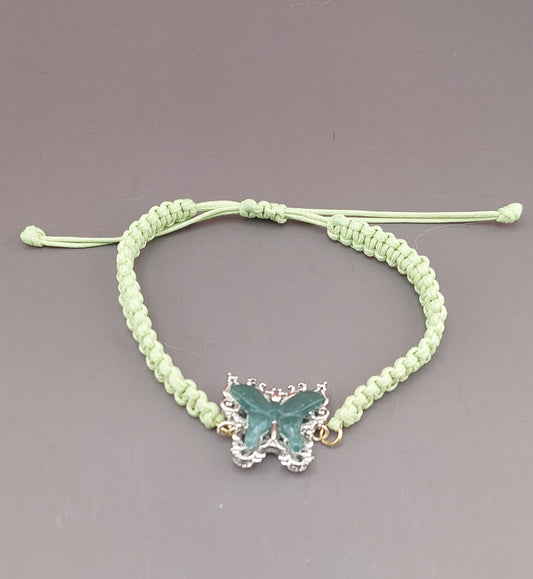 A green macrame anklet with a blue water jade butterfly charm, displayed against a grey background.