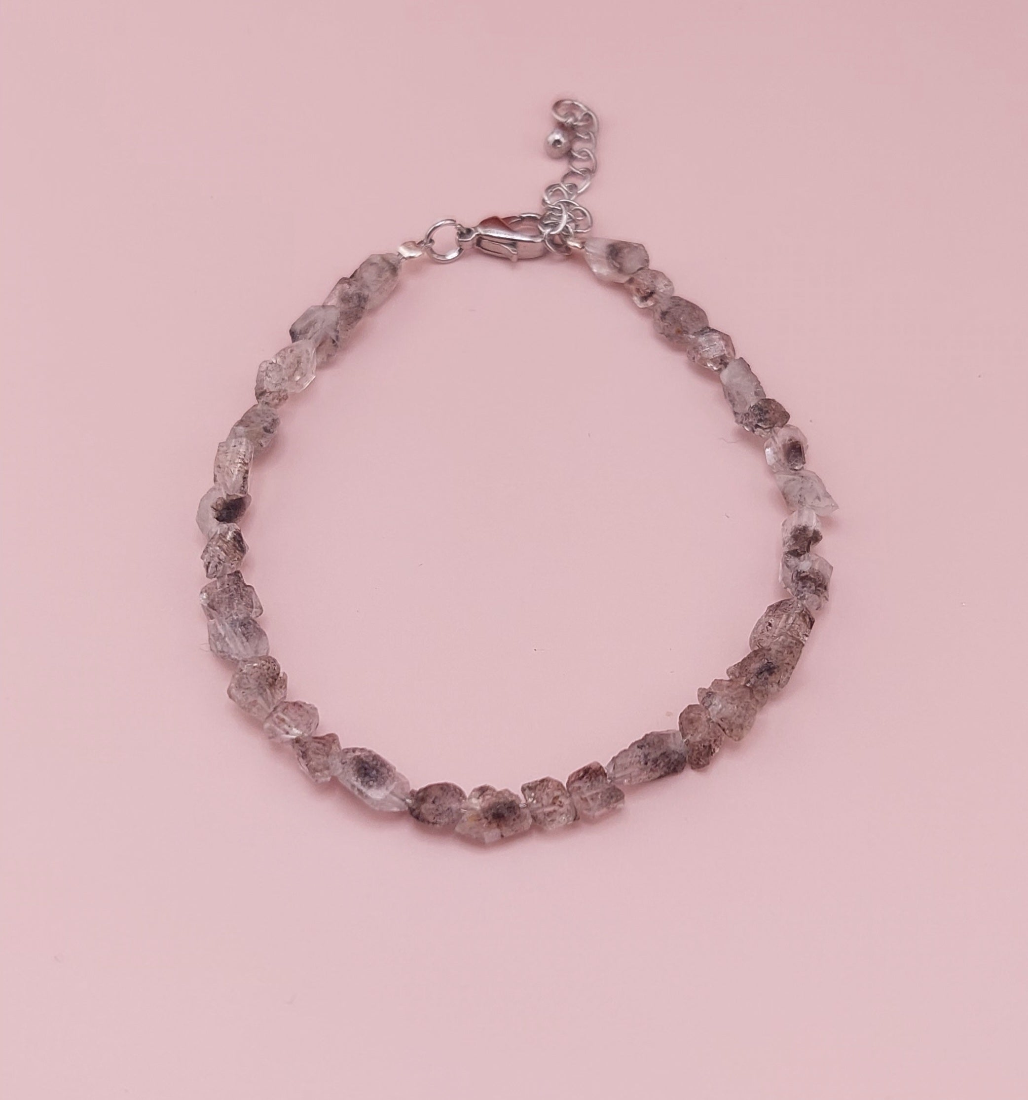 A bracelet made with clear Herkimer diamond stones, featuring a diamond cut design, displayed against a pink background.