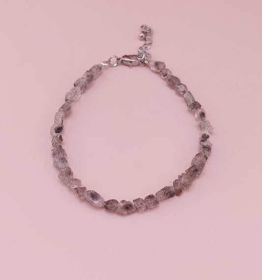 A bracelet made with clear Herkimer diamond stones, featuring a diamond cut design, displayed against a pink background.