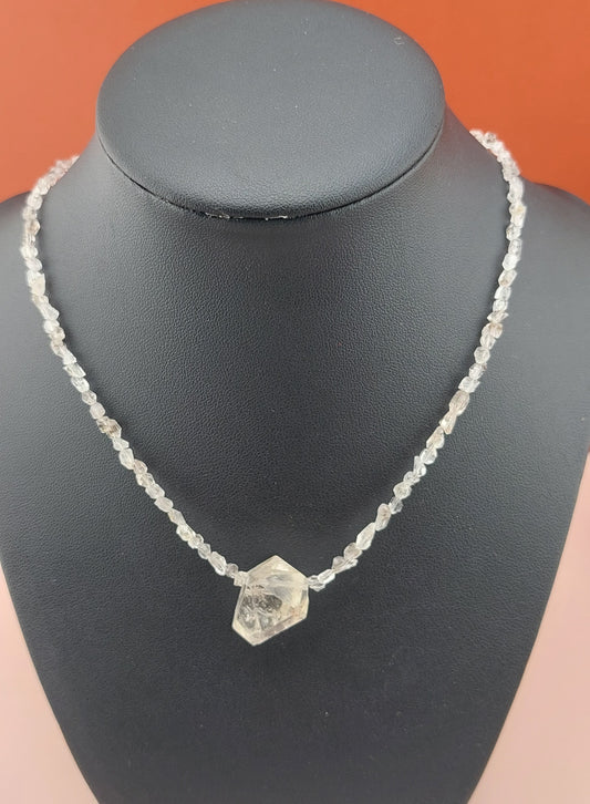 A Herkimer diamond necklace displayed on a mannequin neck stand, featuring a clear stone set in a silver or metallic chain.