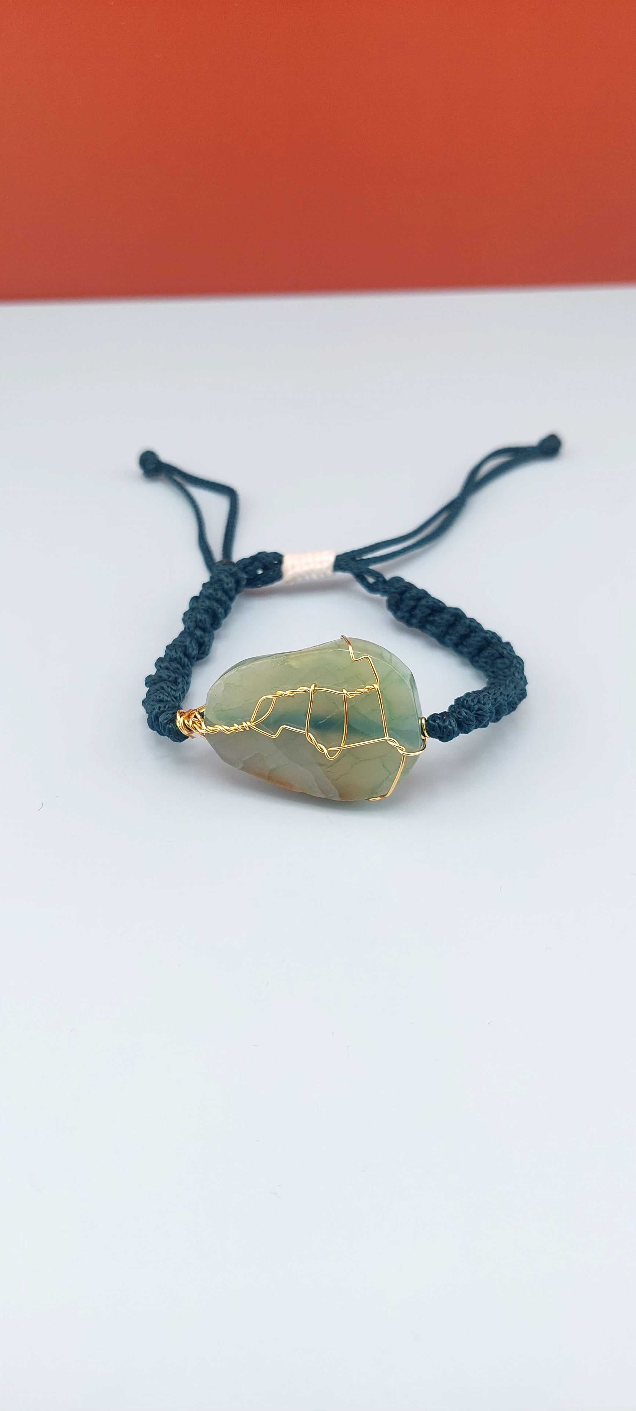 An elegant crackled agate stone macrame bracelet with blue and green strings, displayed against a two-tone background.