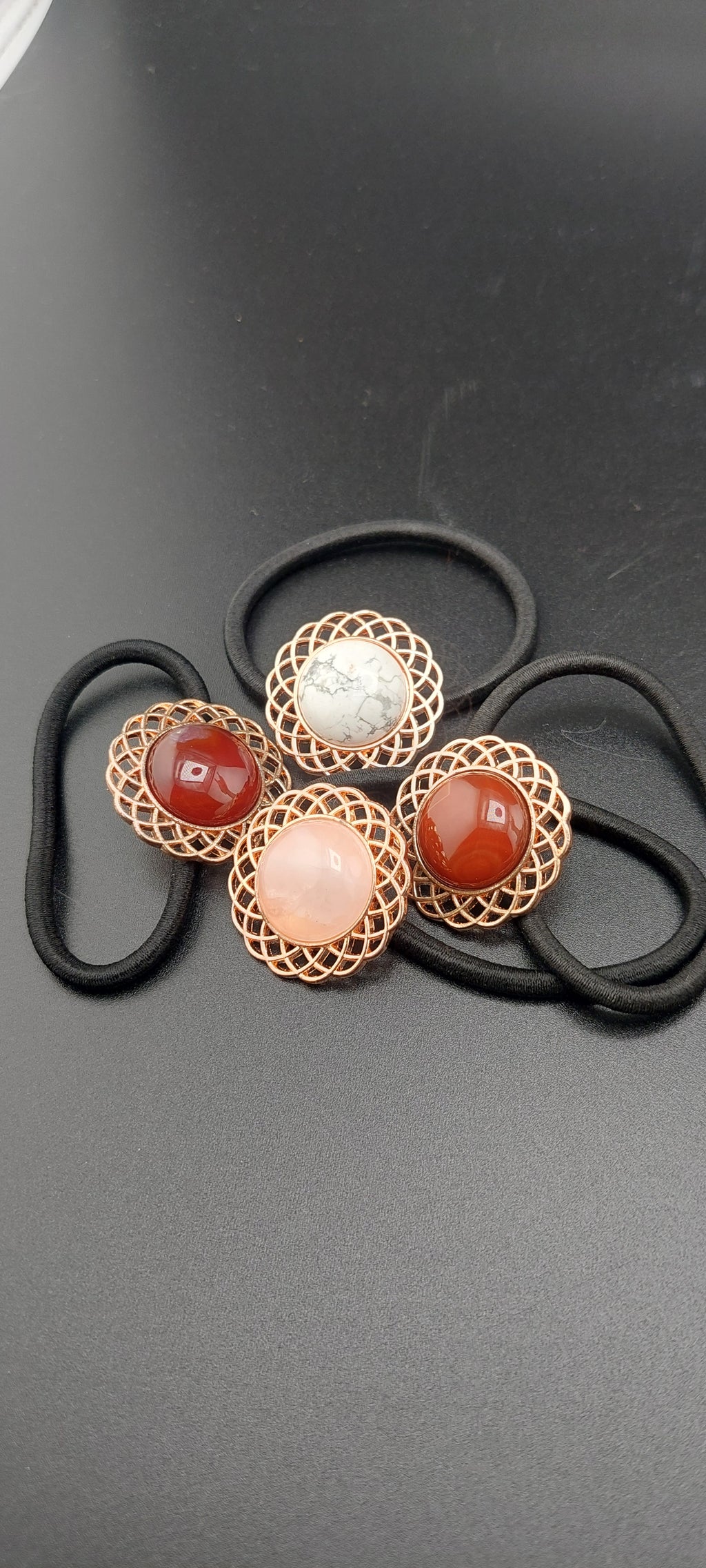 A set of rose gold hair ties with multicolored gemstones and intricate designs on a dark background.
