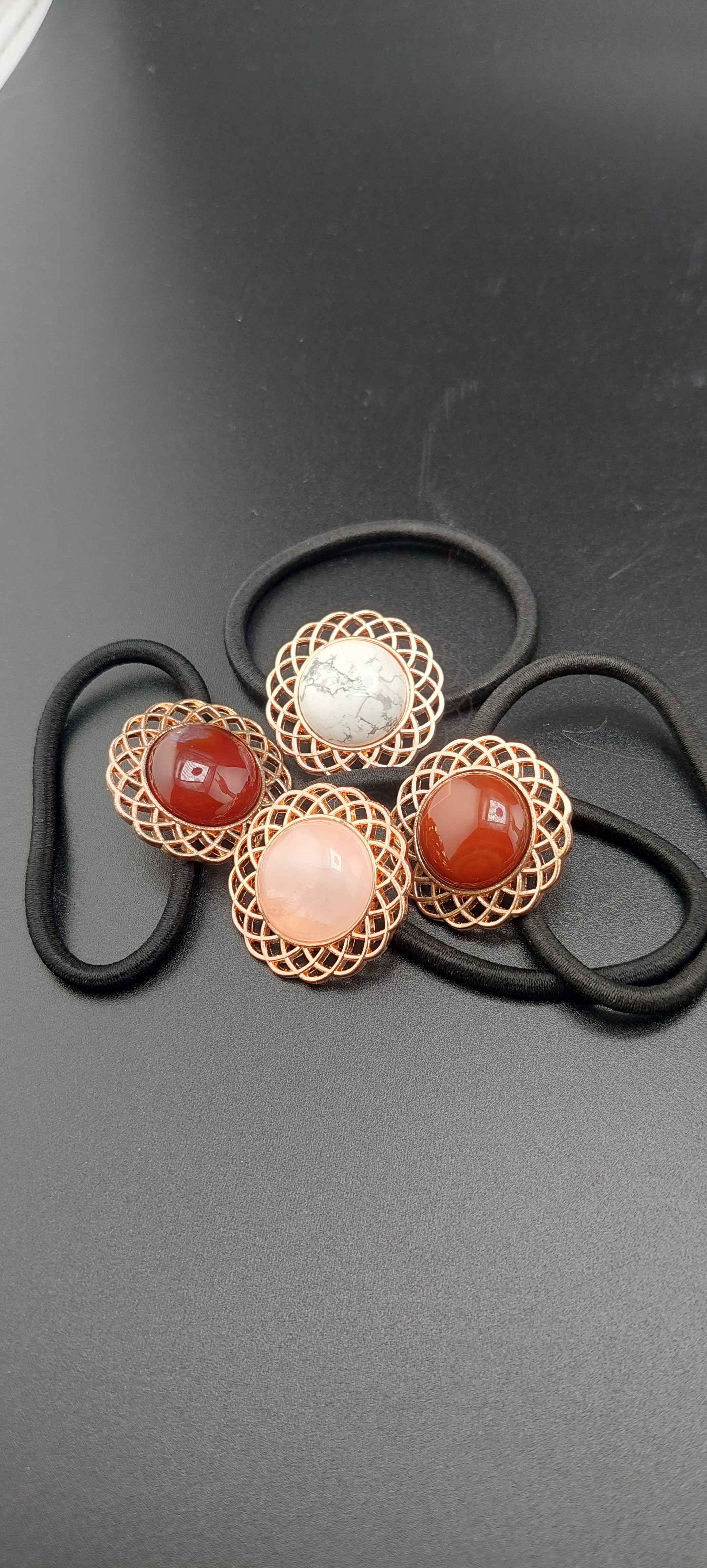 A set of rose gold hair ties with multicolored gemstones and intricate designs on a dark background.