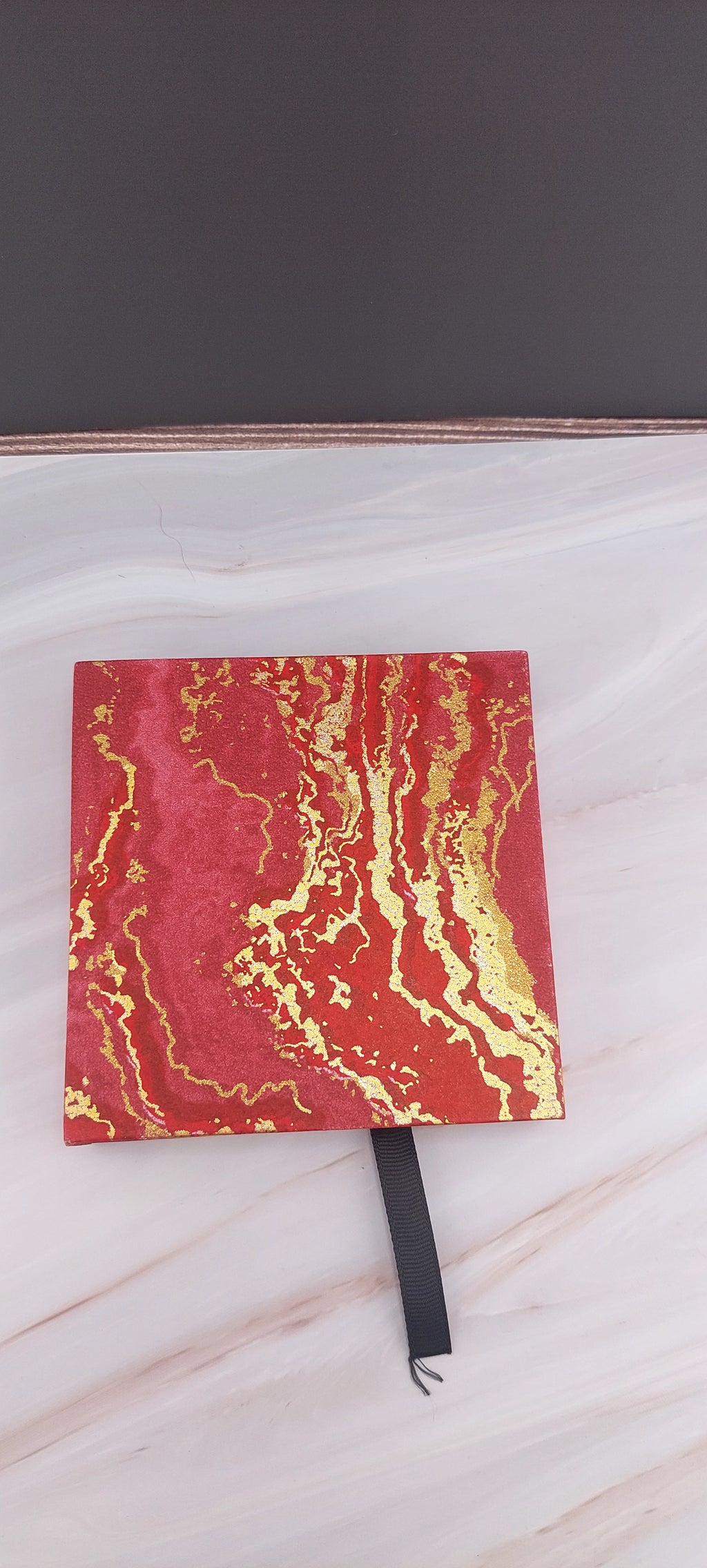 A red and gold bangle box with a sticky texture on the inside, placed on a marble surface.