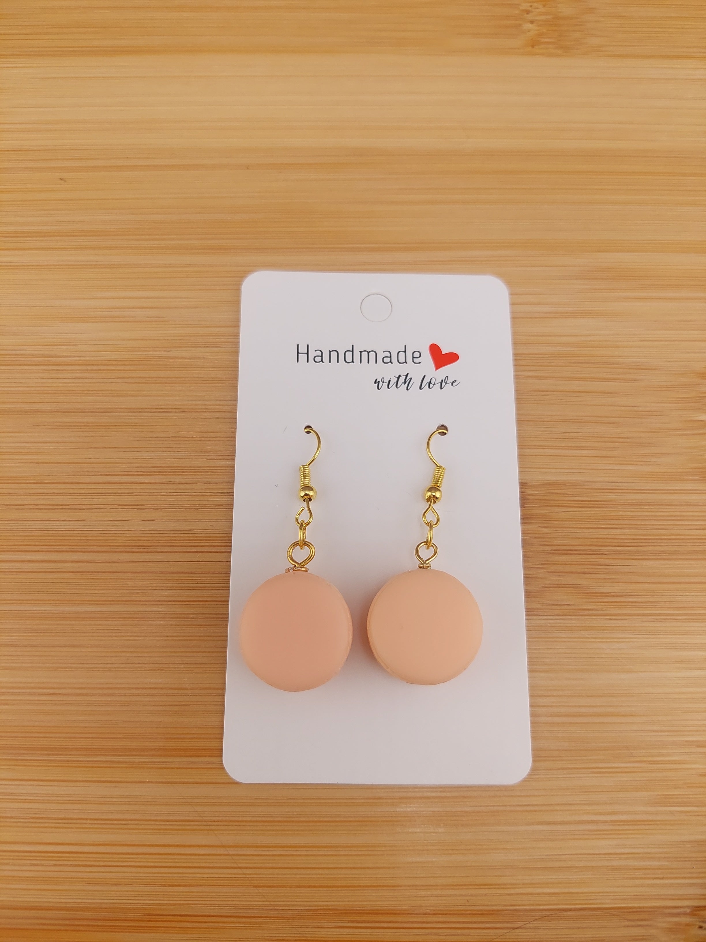 Pair of peach-colored earrings on a 'Handmade with Love' card against a wooden background