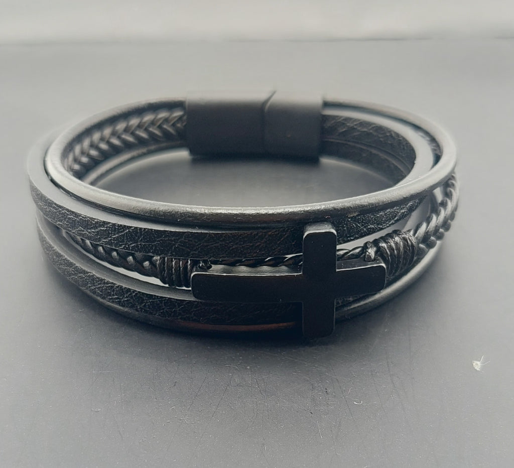 Black leather bracelet with metal cross charm on a gray background