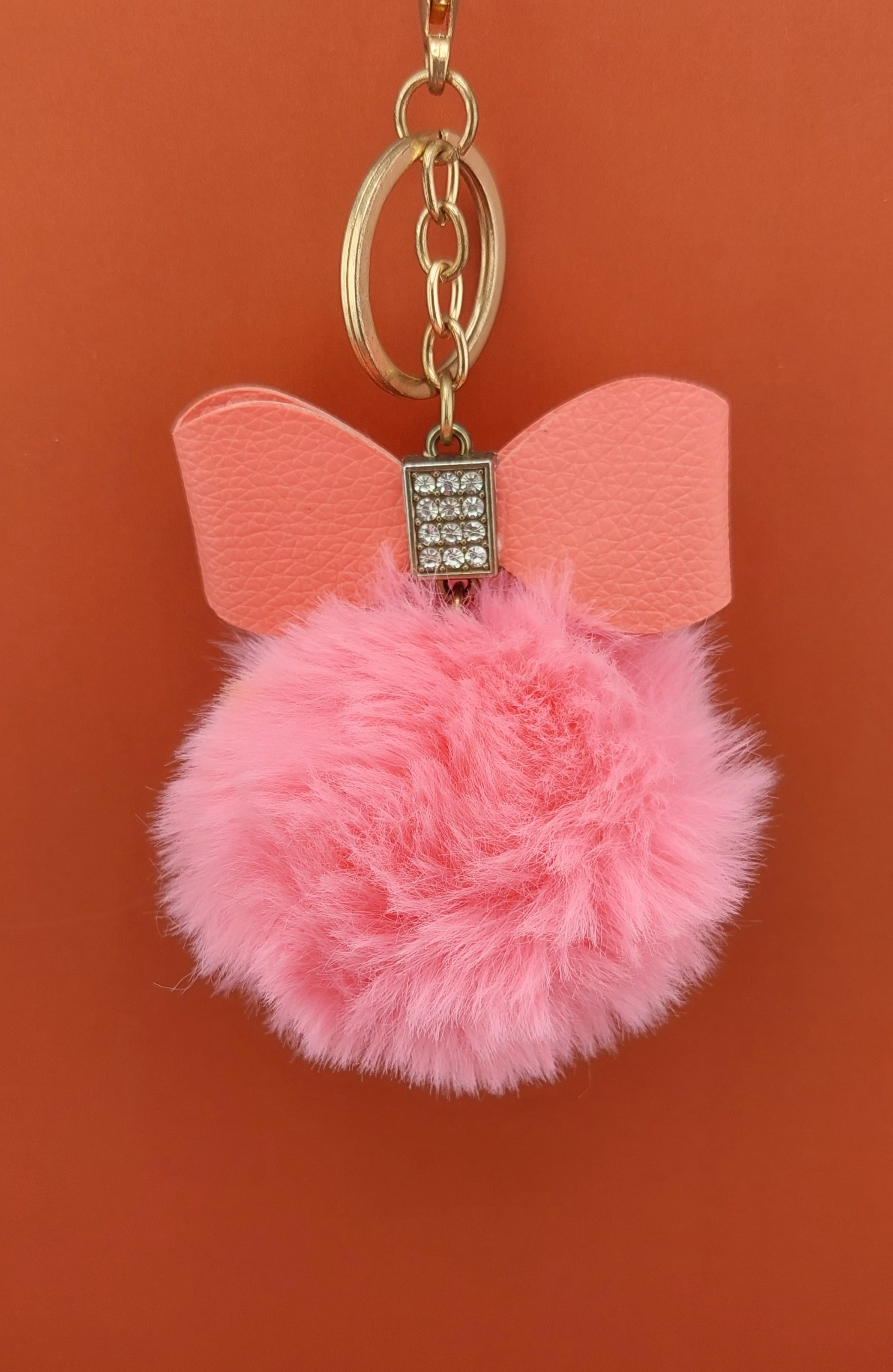 Pink pom-pom keychain with bow and rhinestone on an orange background