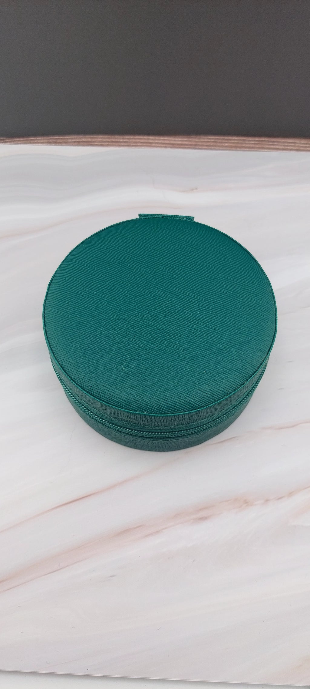 A round jewelry box with a beige interior and patterned exterior, partially open, showing its compartments.