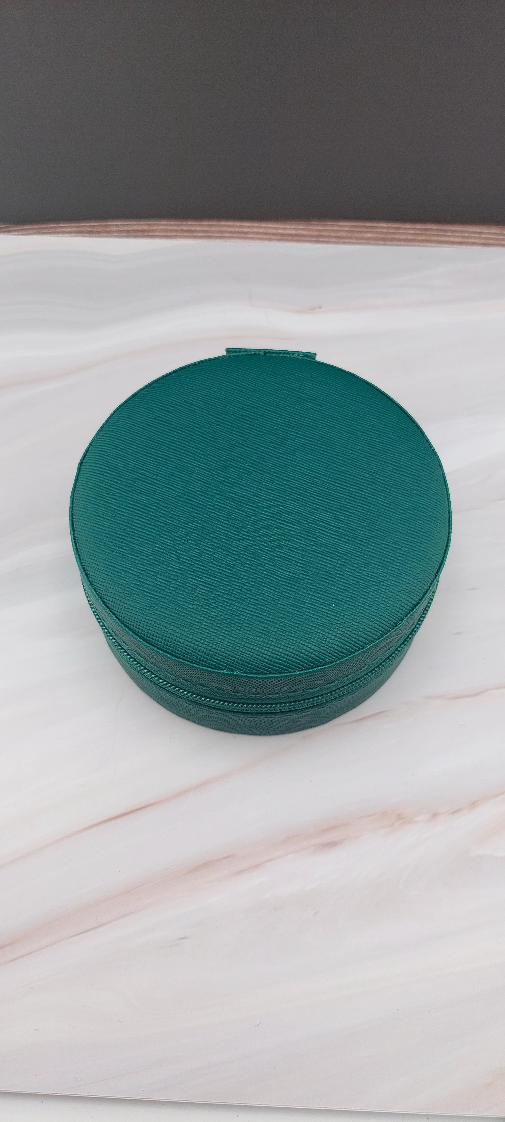 A round jewelry box with a beige interior and patterned exterior, partially open, showing its compartments.
