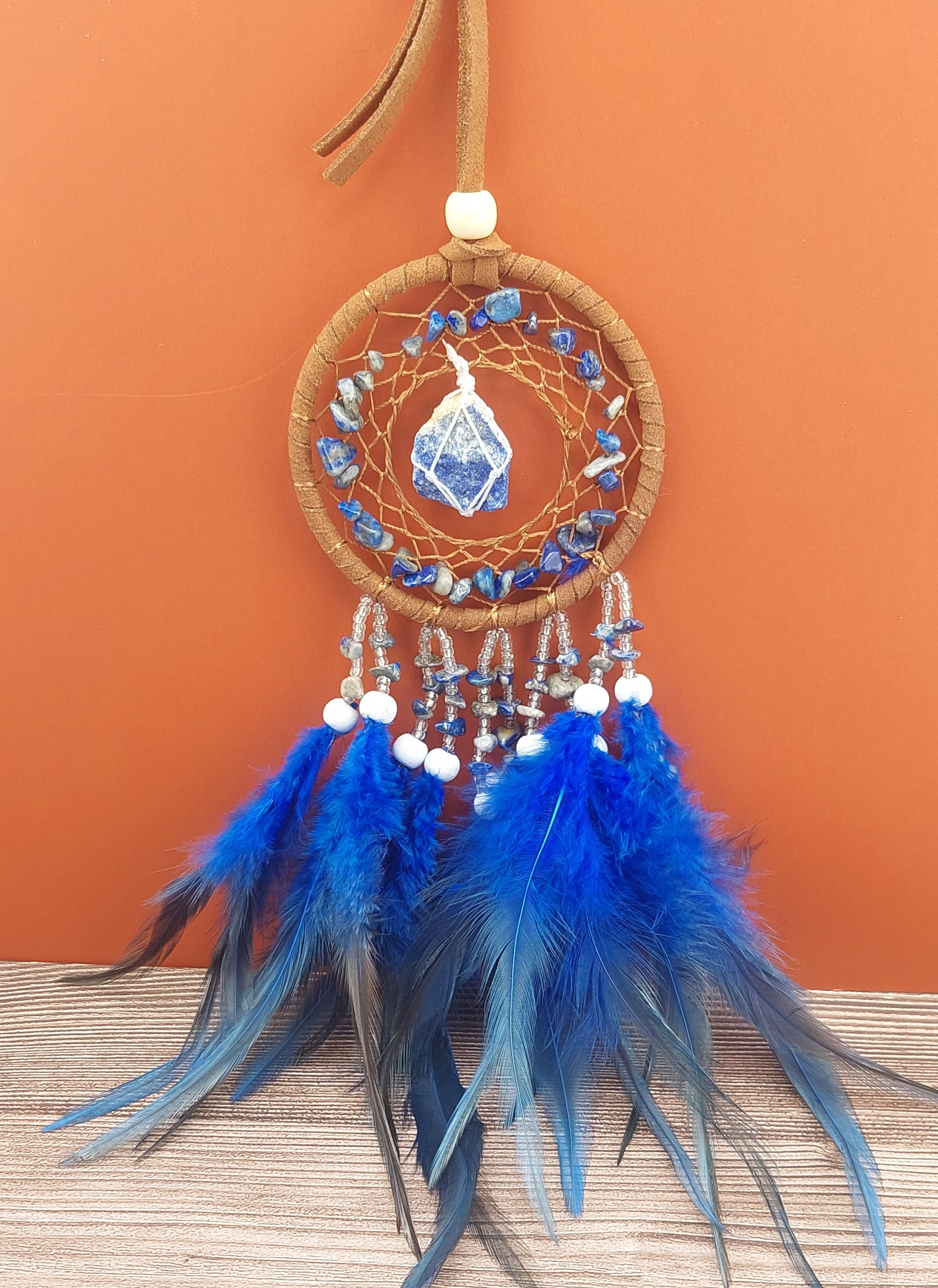 Dreamcatcher with blue feathers and stones on an orange background
