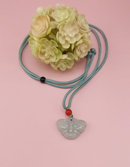 A blue water jade butterfly necklace displayed against a pink background with a decorative flower.