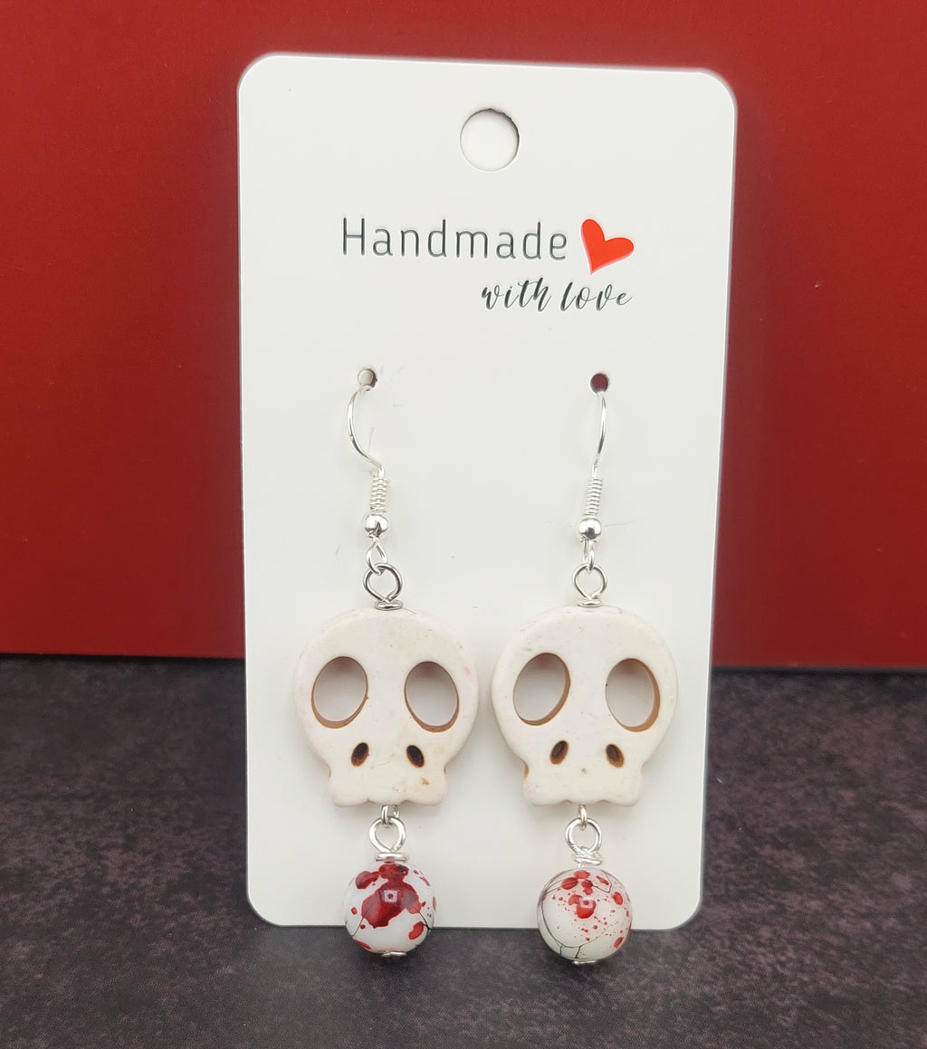 Skull-shaped earrings on a 'Handmade with Love' card against a red background