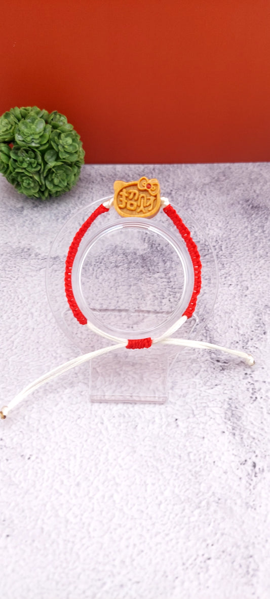 A red and white macrame bracelet with a Hello Kitty charm on a clear display stand against a two-tone background.
