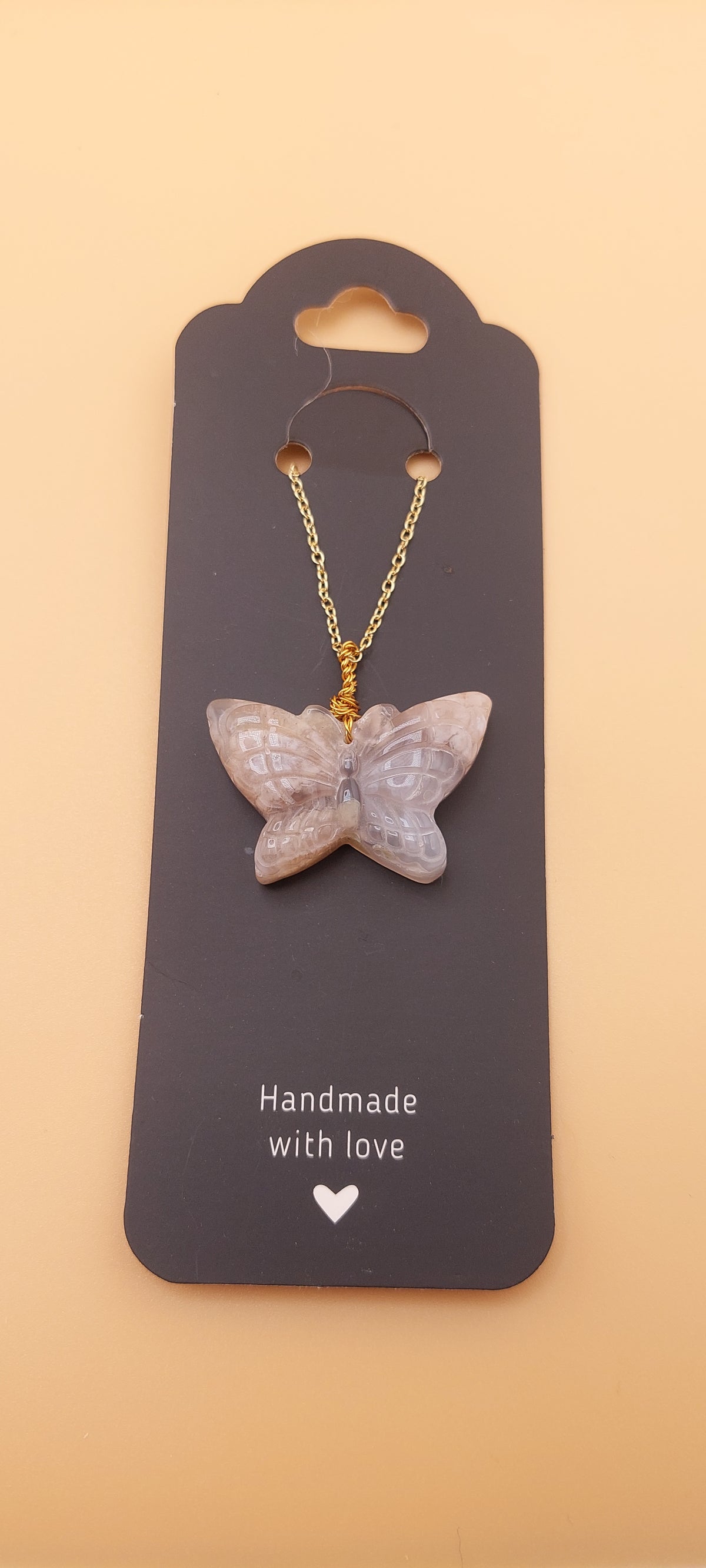 A butterfly-shaped necklace made of flower Agate stone, displayed on a card with the text 'Handmade with love'.